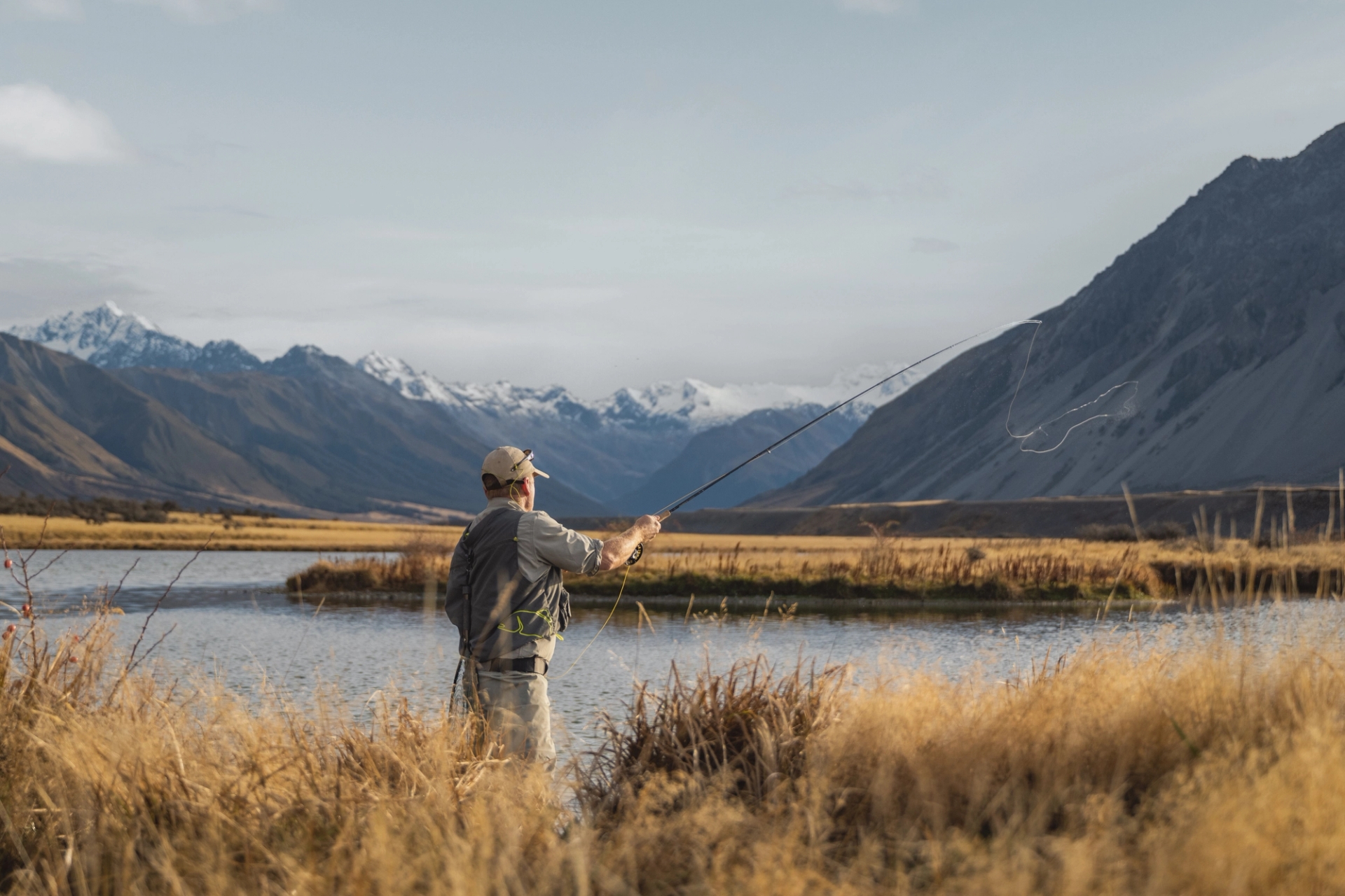 A man fly fishing with a view on the alps in the background.