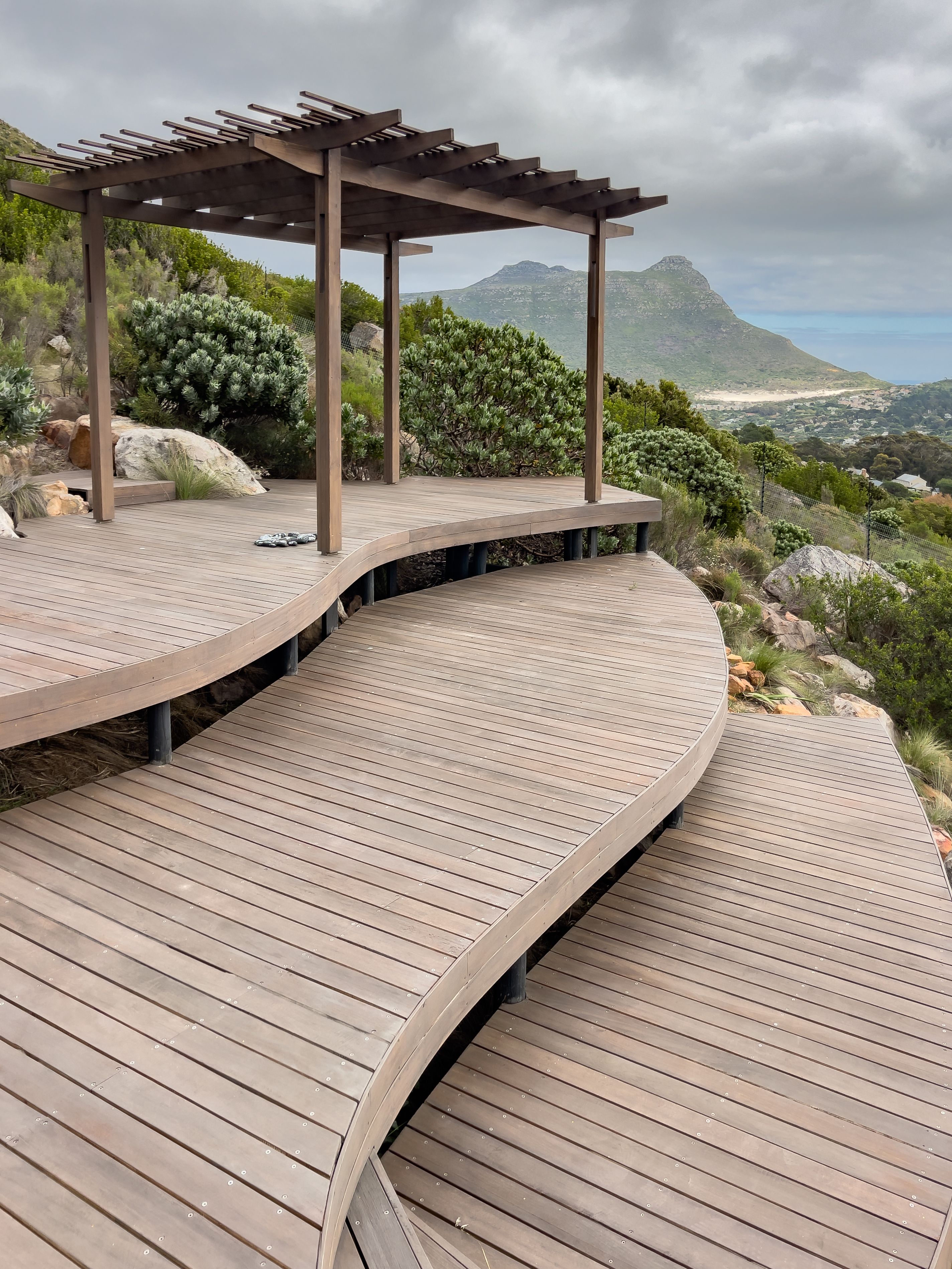 Curved wooden gazebo deck with pergola at the summit of the property, looking out across the valley to the sea