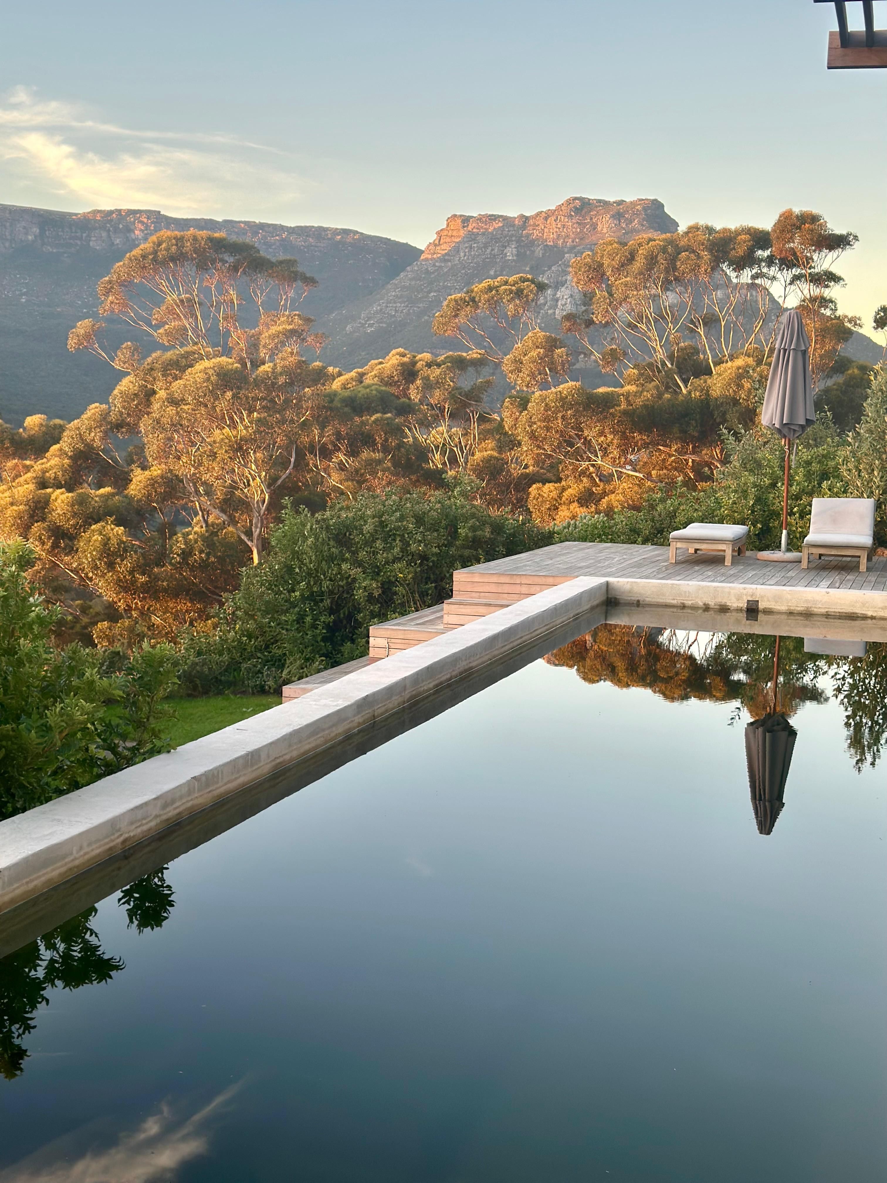 The lap pool at golden hour, gum trees and the Skoorsteenberg ridge lit behind it.