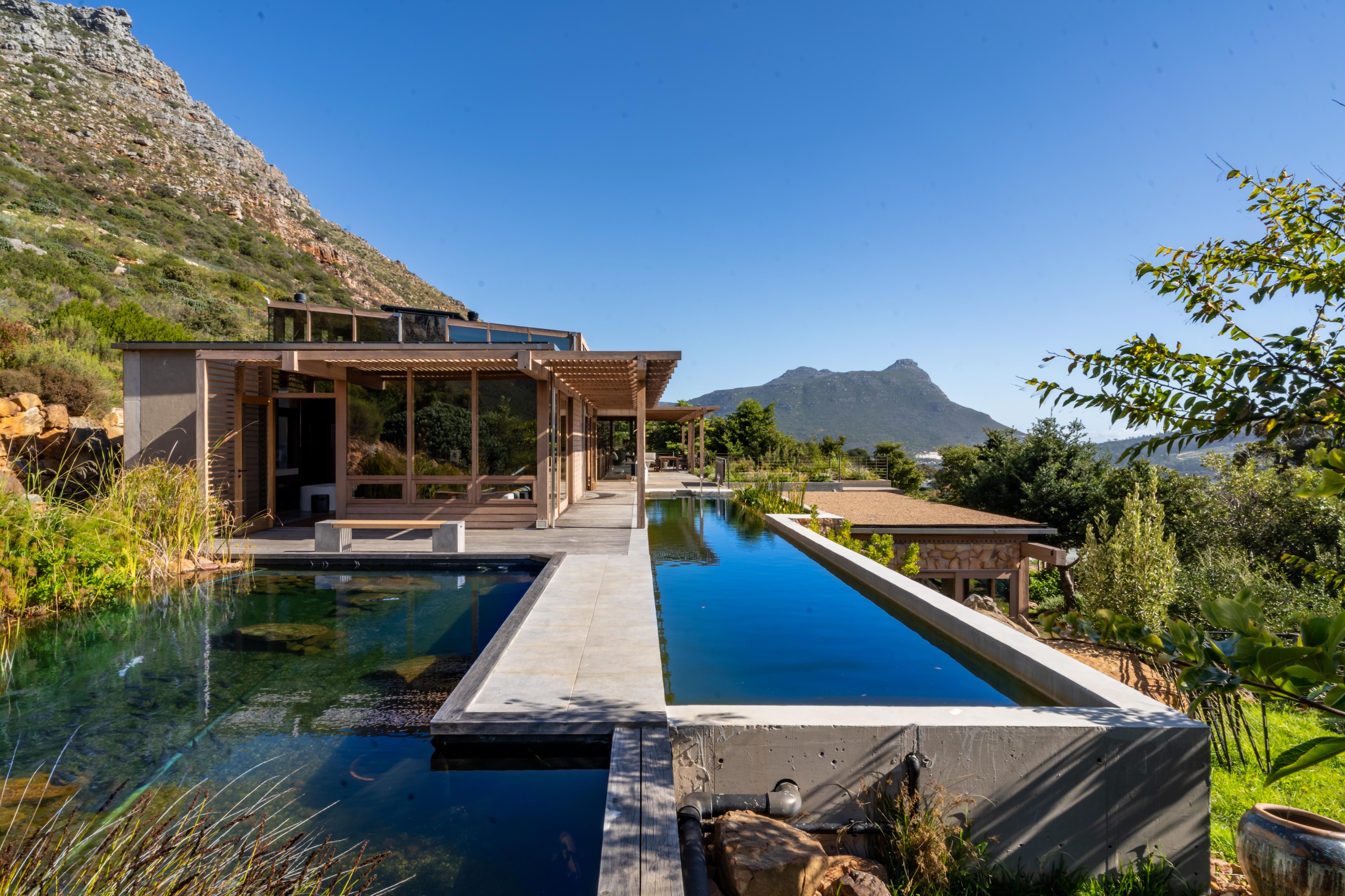 Postcard-wide view of the 20-metre biofiltration lap pool, the deck, the house, and the full mountain panorama