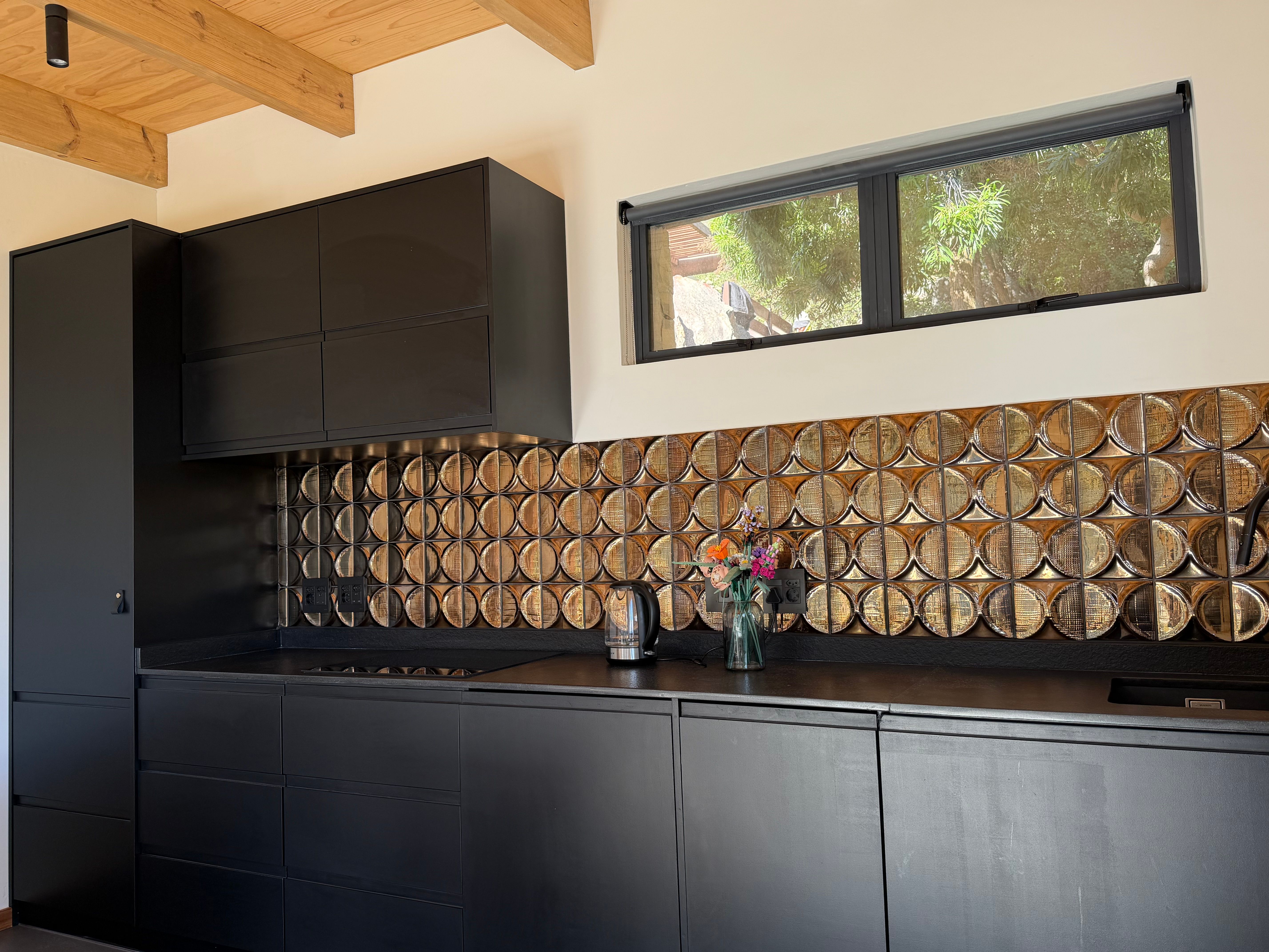 Cottage kitchen interior: black cabinetry, woven-pattern tile backsplash, flowers on the counter