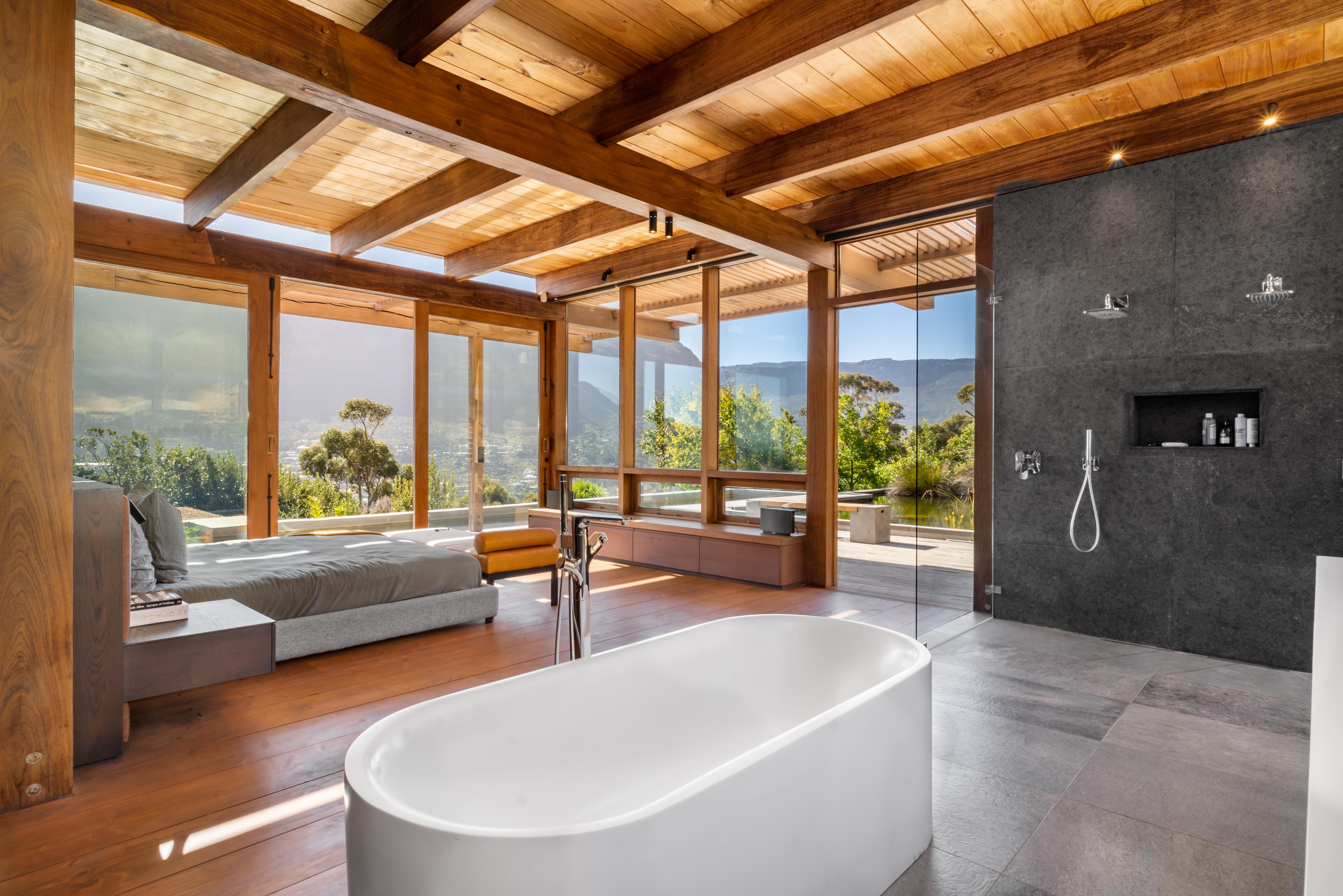 Open-plan master suite: freestanding bathtub, bed, and floor-to-ceiling glass opening to the mountain