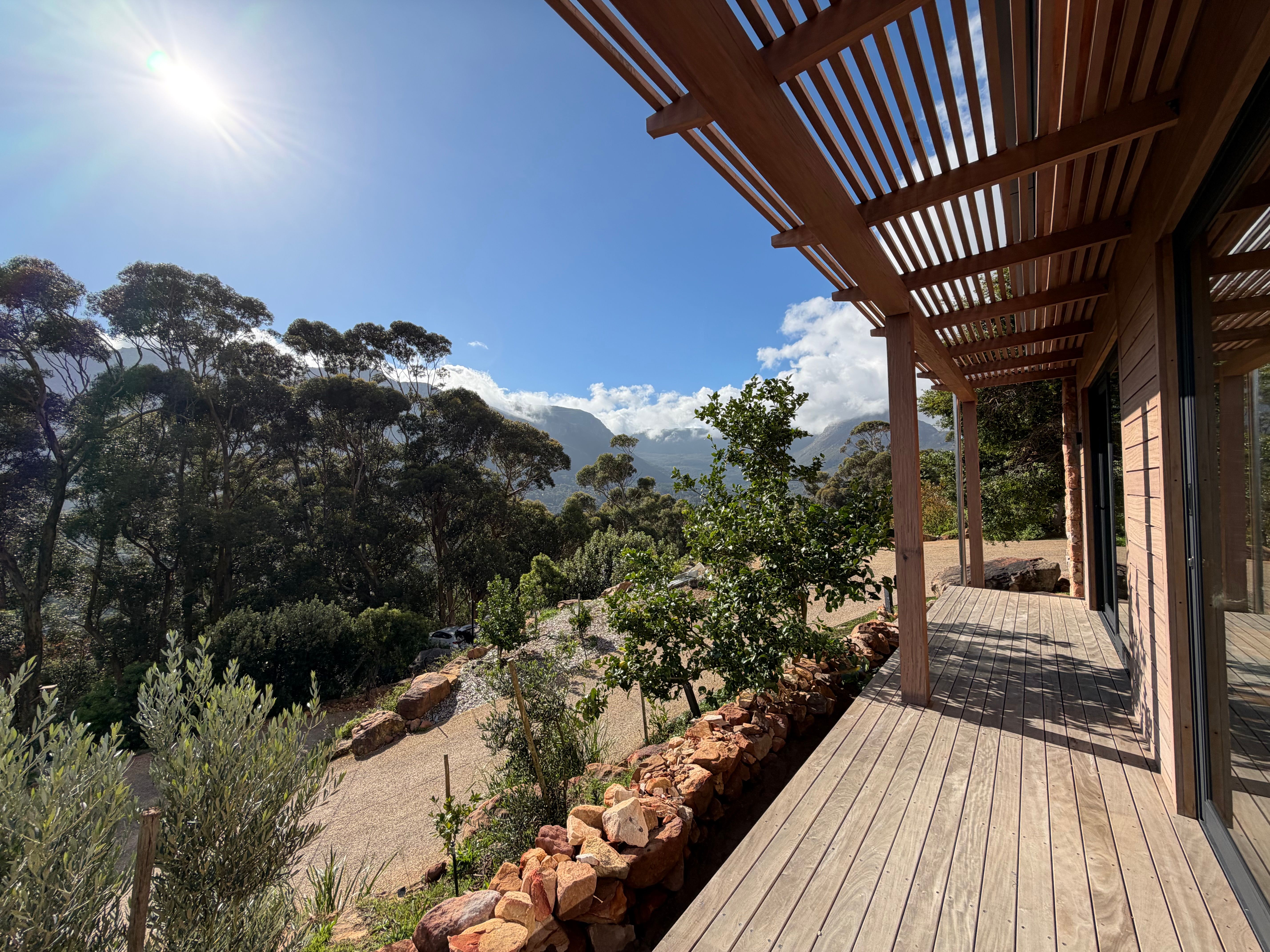 Cottage deck at golden hour, pergola overhead, sun-flare, fynbos and mountain visible