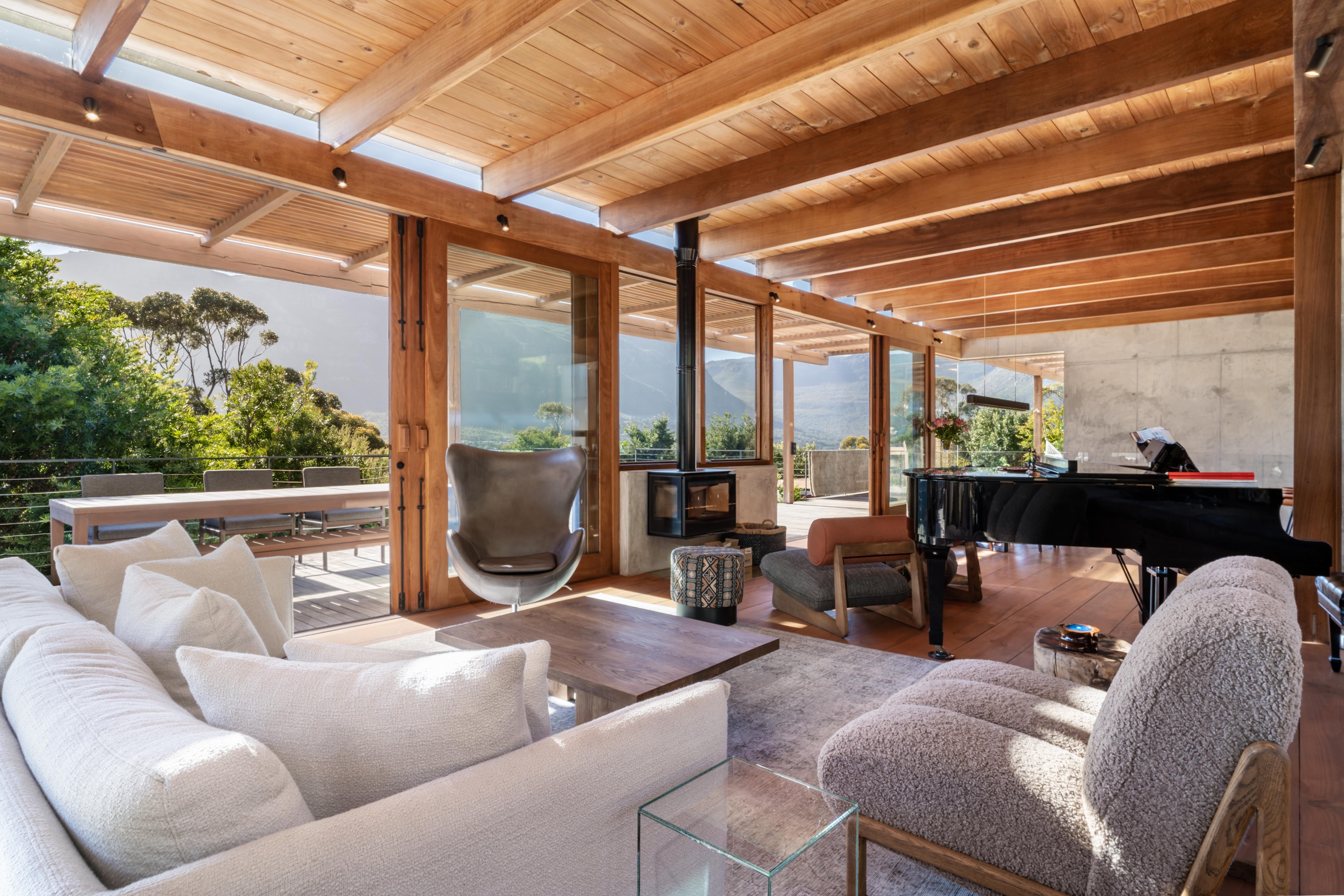 Living room: grand piano + sofas + wood-fired stove + mountain through the glass