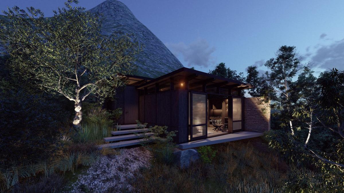 Writers Cottage at night: warm interior glow through the glass facade, soft uplight on a tree, the mountain rising in the deep-blue twilight