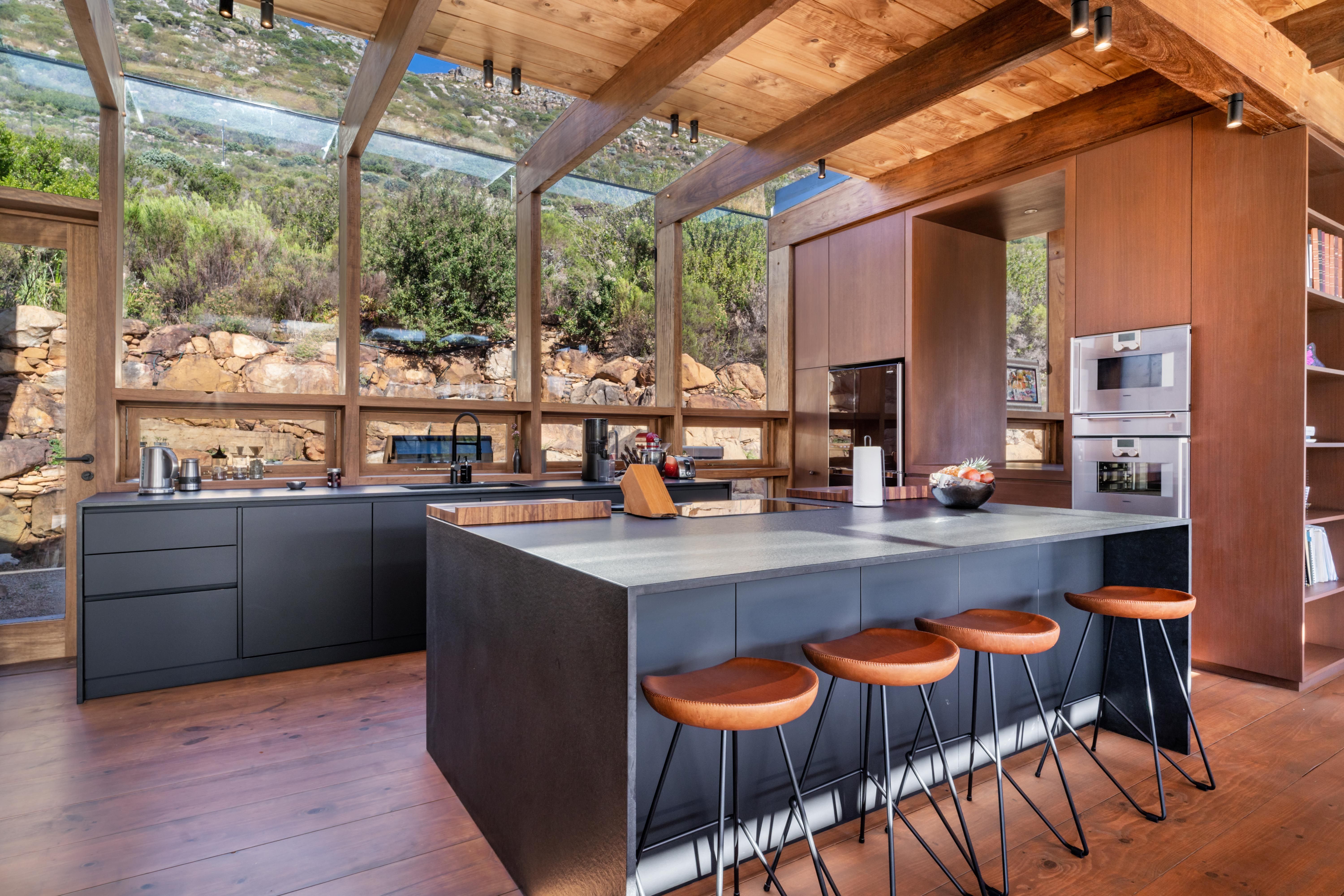 Kitchen interior: dark cabinetry on Zimbabwean Black Granite, butcher-block island, full-height glass to the fynbos slope