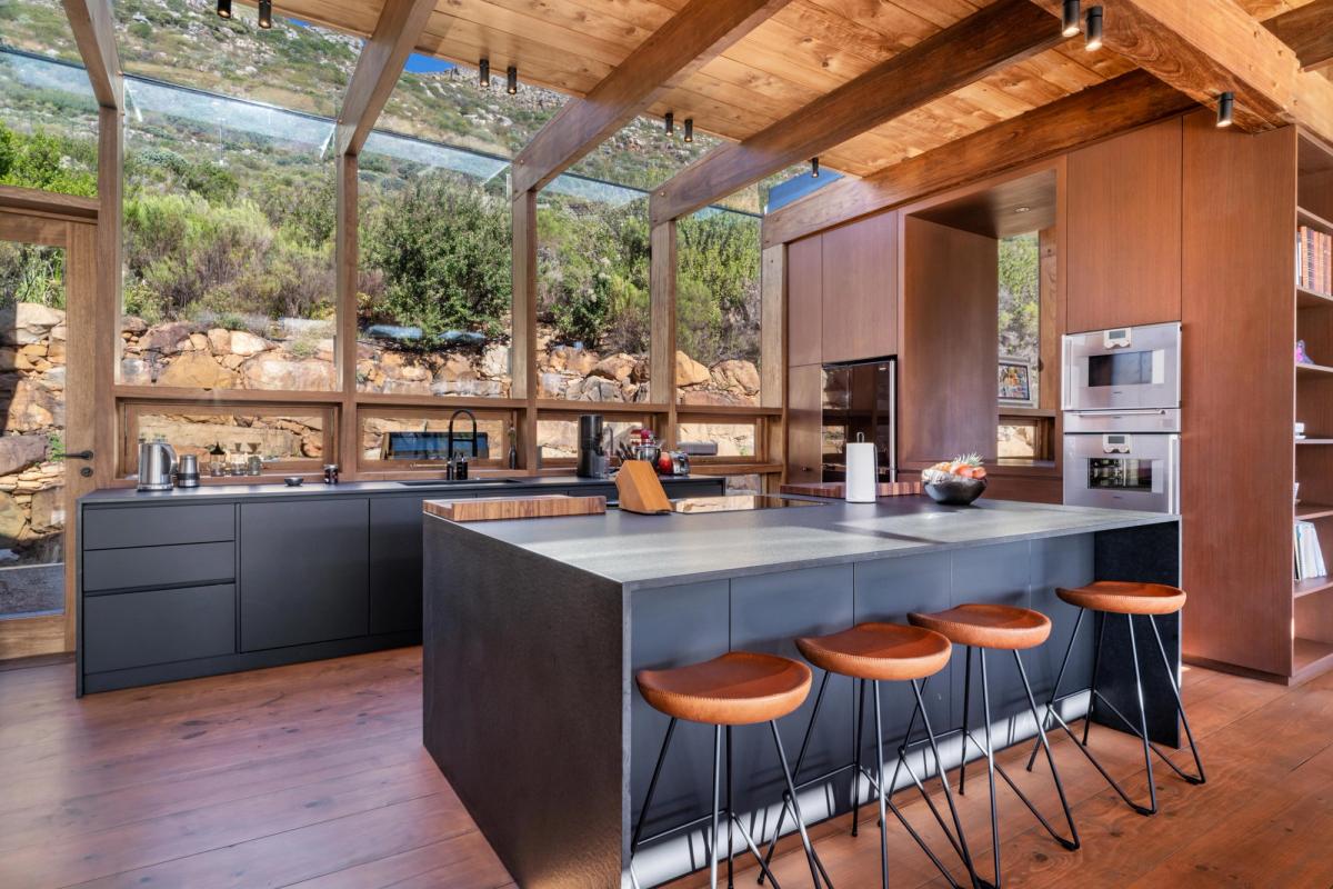 Kitchen interior: dark cabinetry on Zimbabwean Black Granite, butcher-block island, full-height glass to the fynbos slope