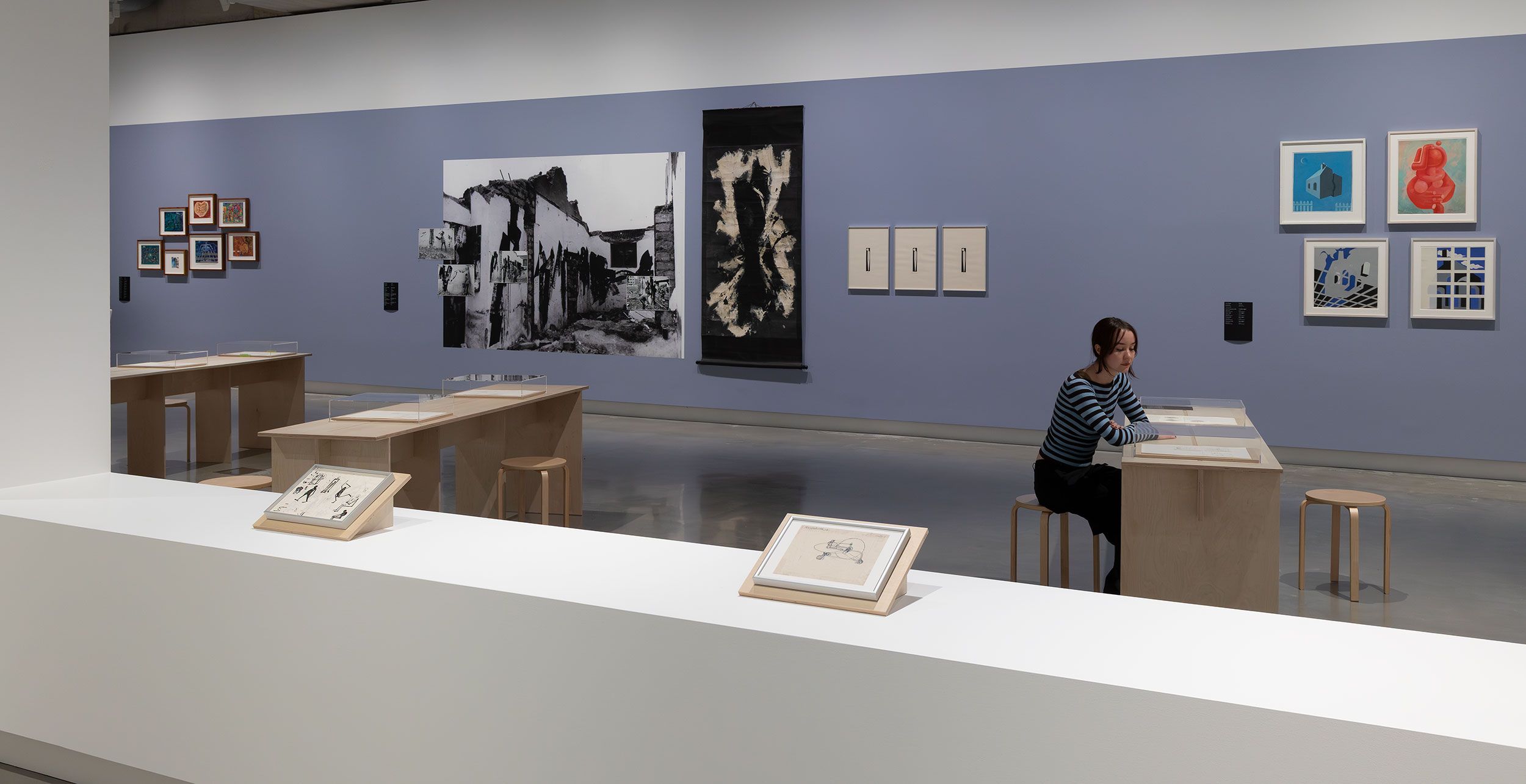 A person sitting at a wooden table in a contemporary art gallery.
