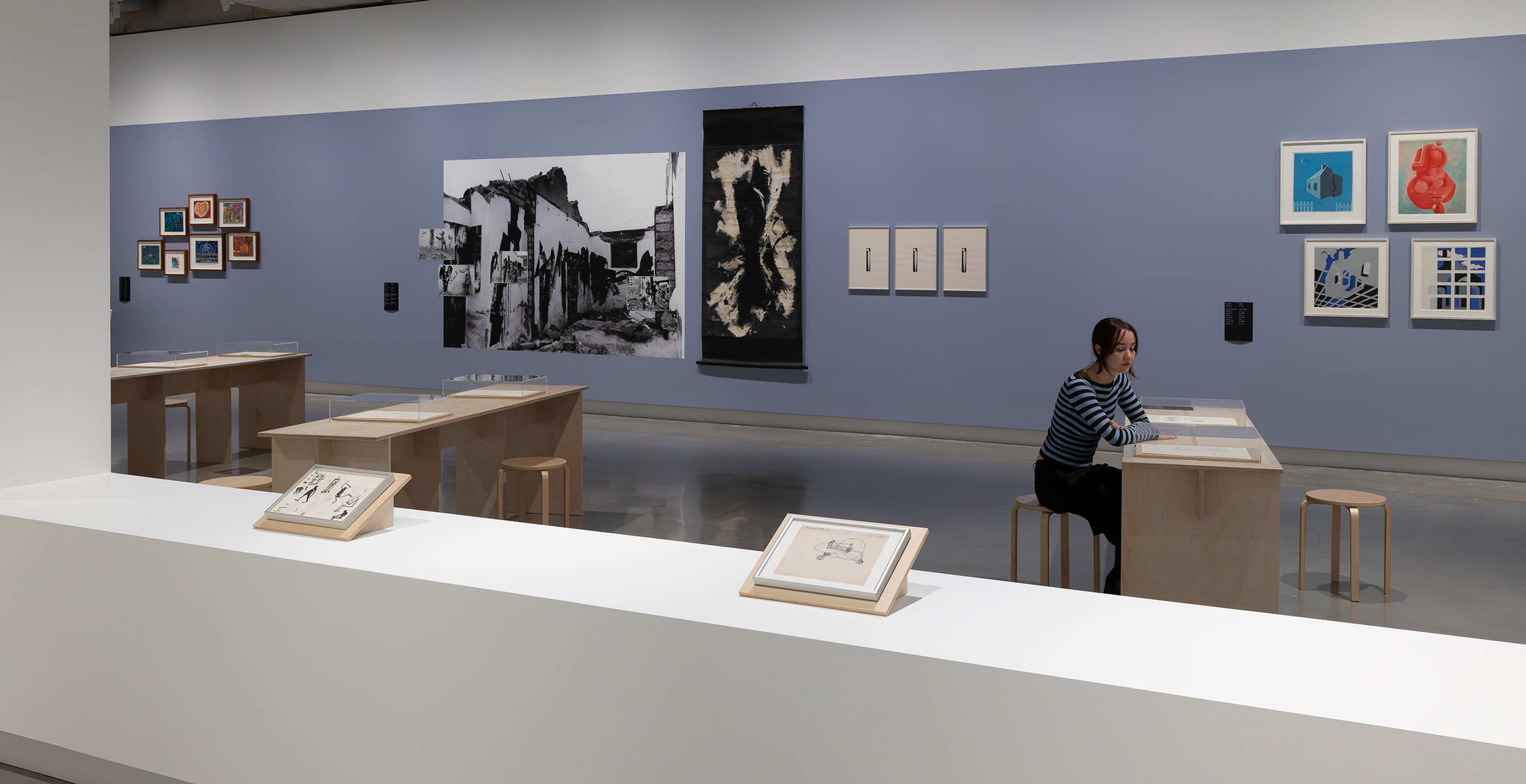 A person sitting at a wooden table in a contemporary art gallery.
