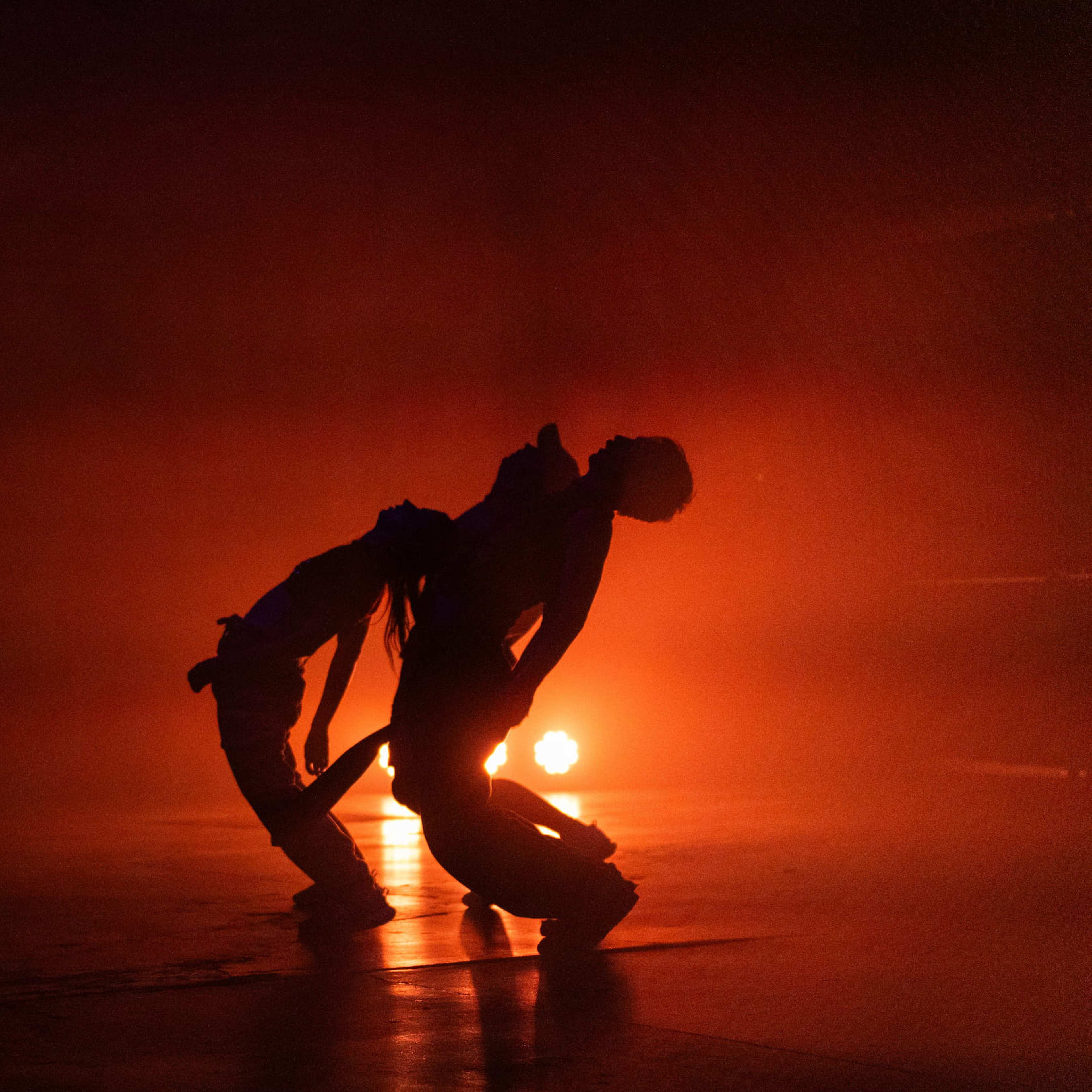 Two dancers bend backwards in front of a red light on a gallery floor