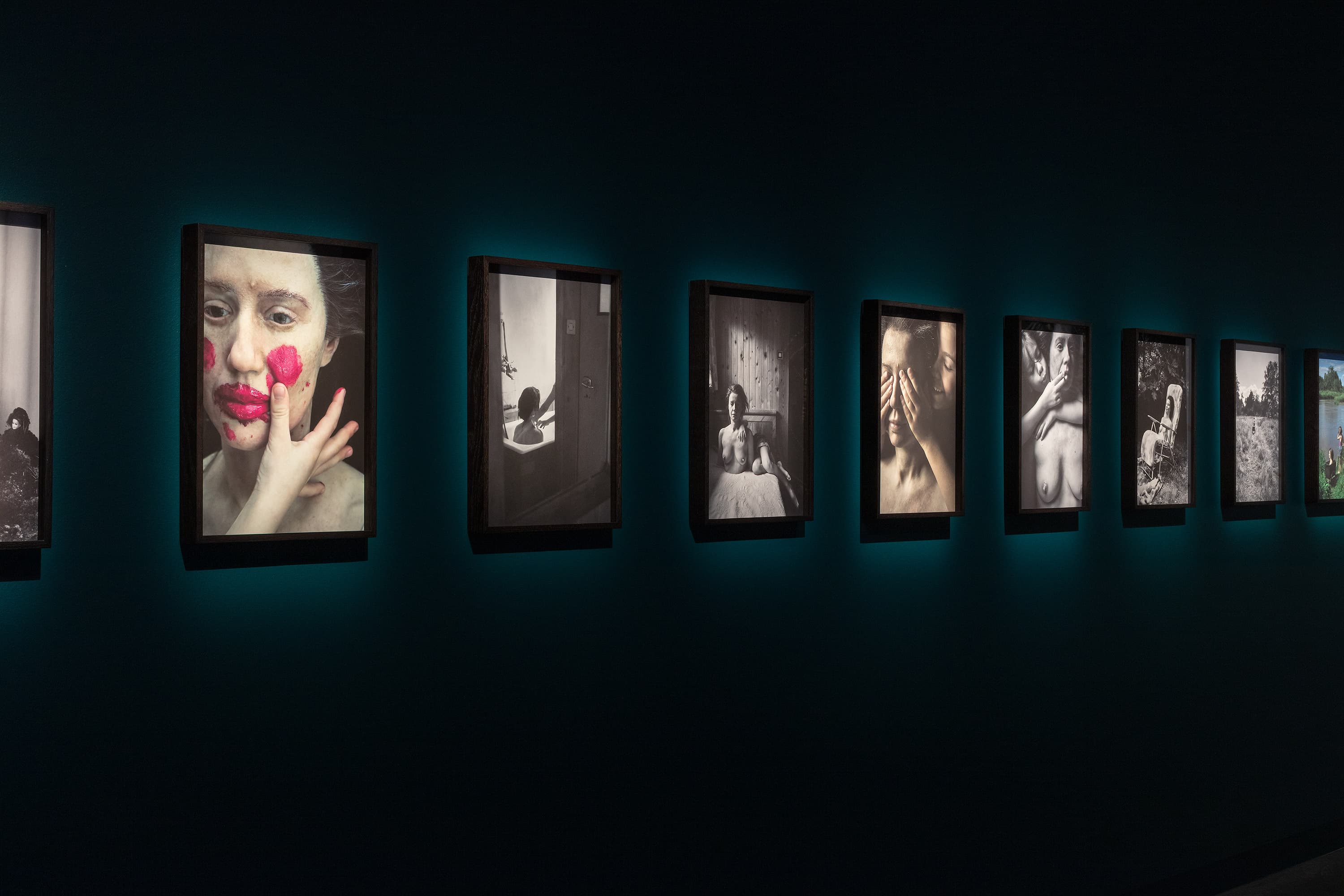 A row of framed black-and-white and color photographs displayed on a dark wall, each photo individually lit and featuring expressive portraits and artistic scenes.