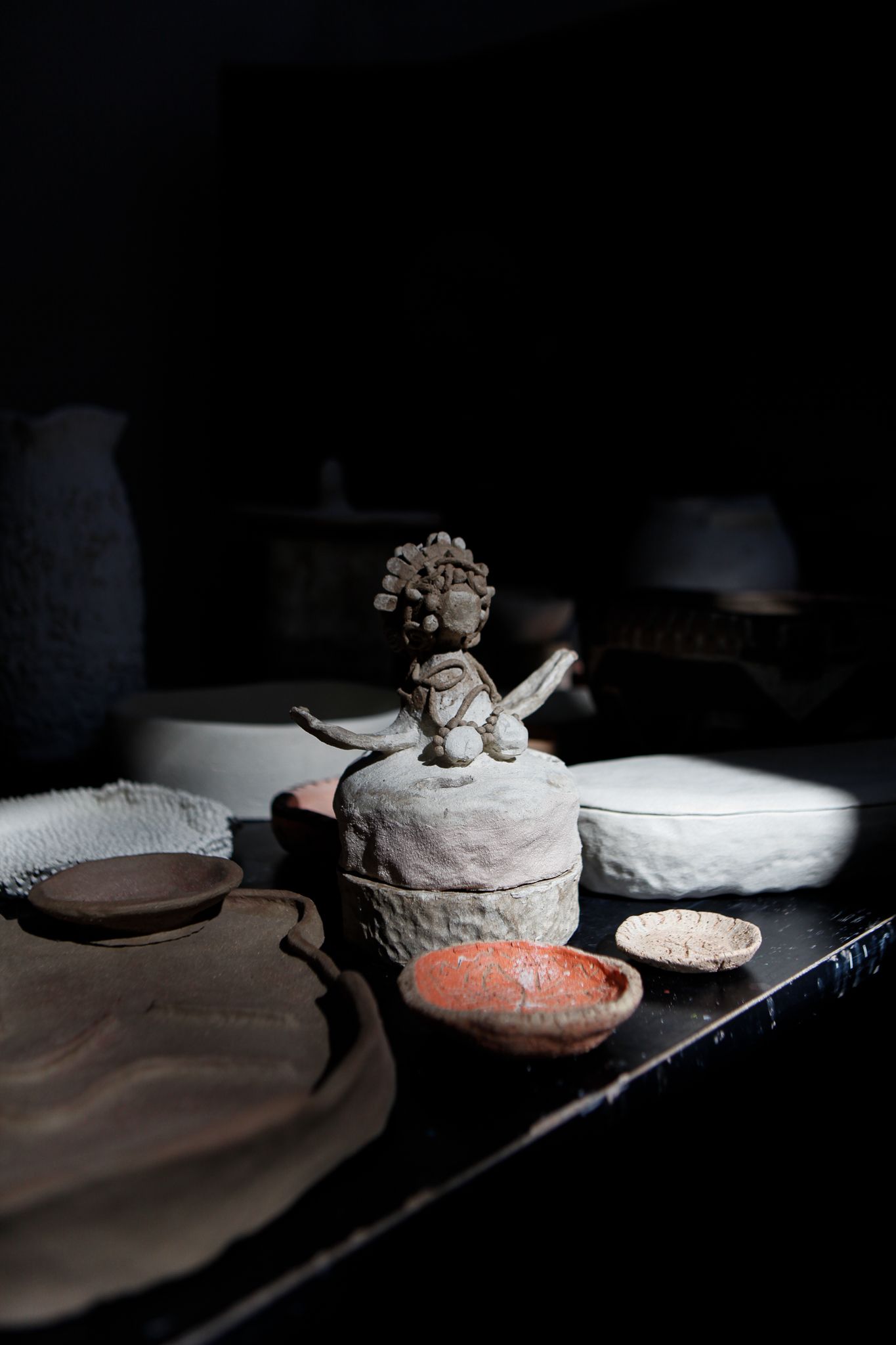 A group of ancient pottery vessels, including a textured clay jar, a white ribbed bowl, and other earthenware, displayed against a dark background with dramatic lighting highlighting their surfaces.