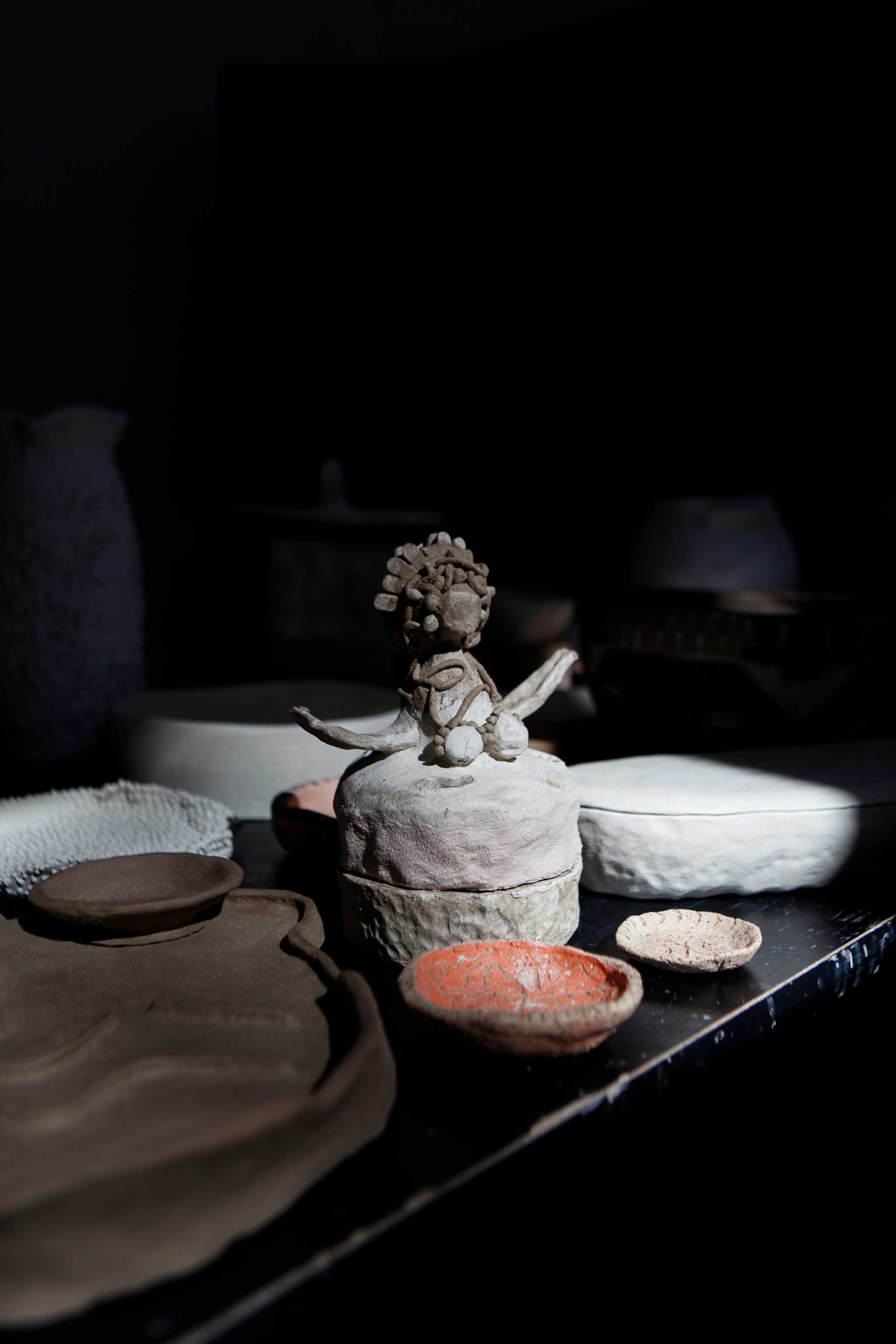 A group of ancient pottery vessels, including a textured clay jar, a white ribbed bowl, and other earthenware, displayed against a dark background with dramatic lighting highlighting their surfaces.