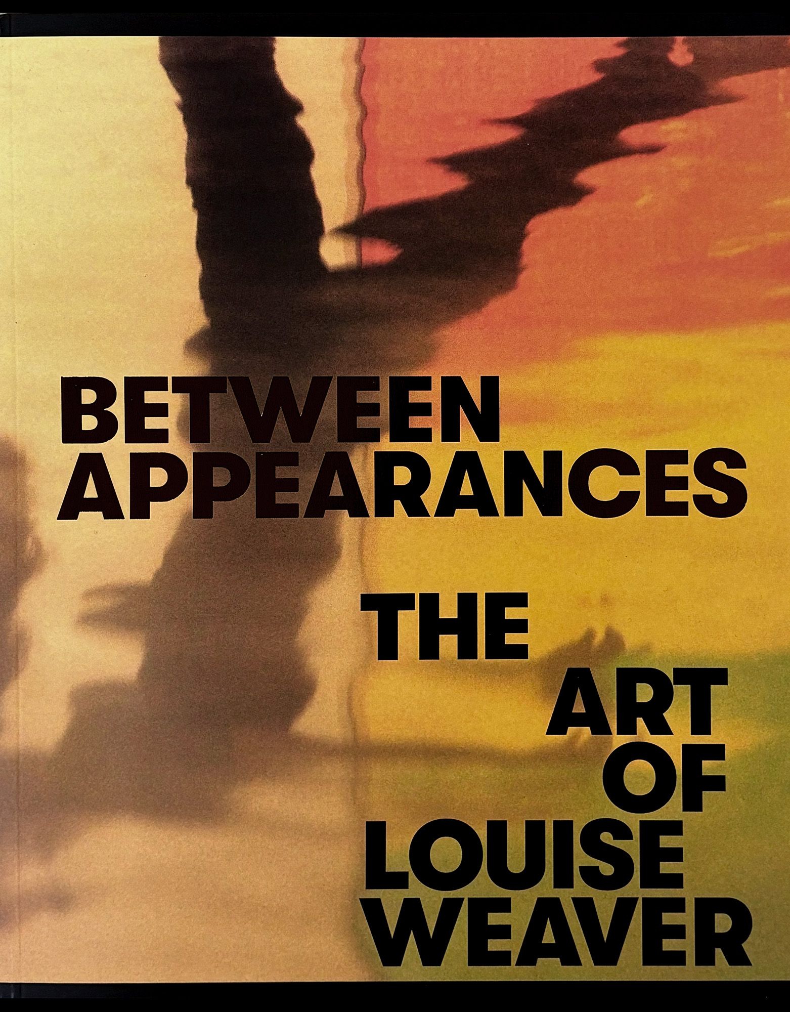Book cover featuring abstract, yellow and orange watercolor with shadowy shapes. Text reads: BETWEEN APPEARANCES THE ART OF LOUISE WEAVER.