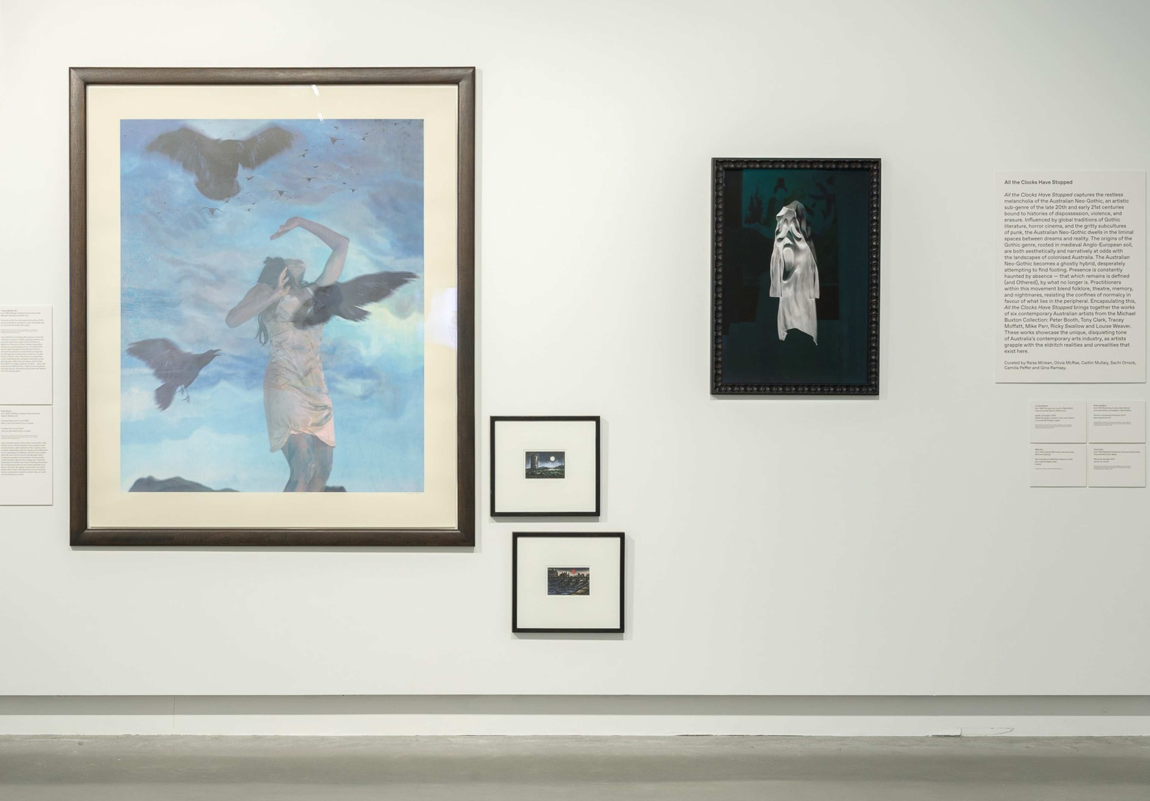 A gallery wall displays four artworks: a large painting of a woman with crows, a smaller portrait of a woman with a covered face, and two small landscape photographs, plus museum labels with descriptions.