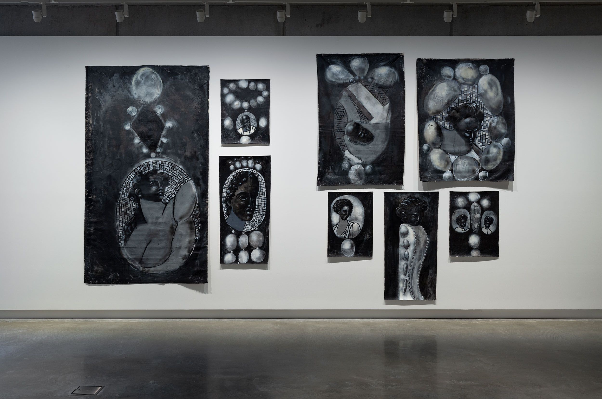 A gallery wall displays seven monochrome artworks featuring abstract and stylized portraits, circular patterns, and textured elements, each in shades of black, white, and gray, with a polished concrete floor below.