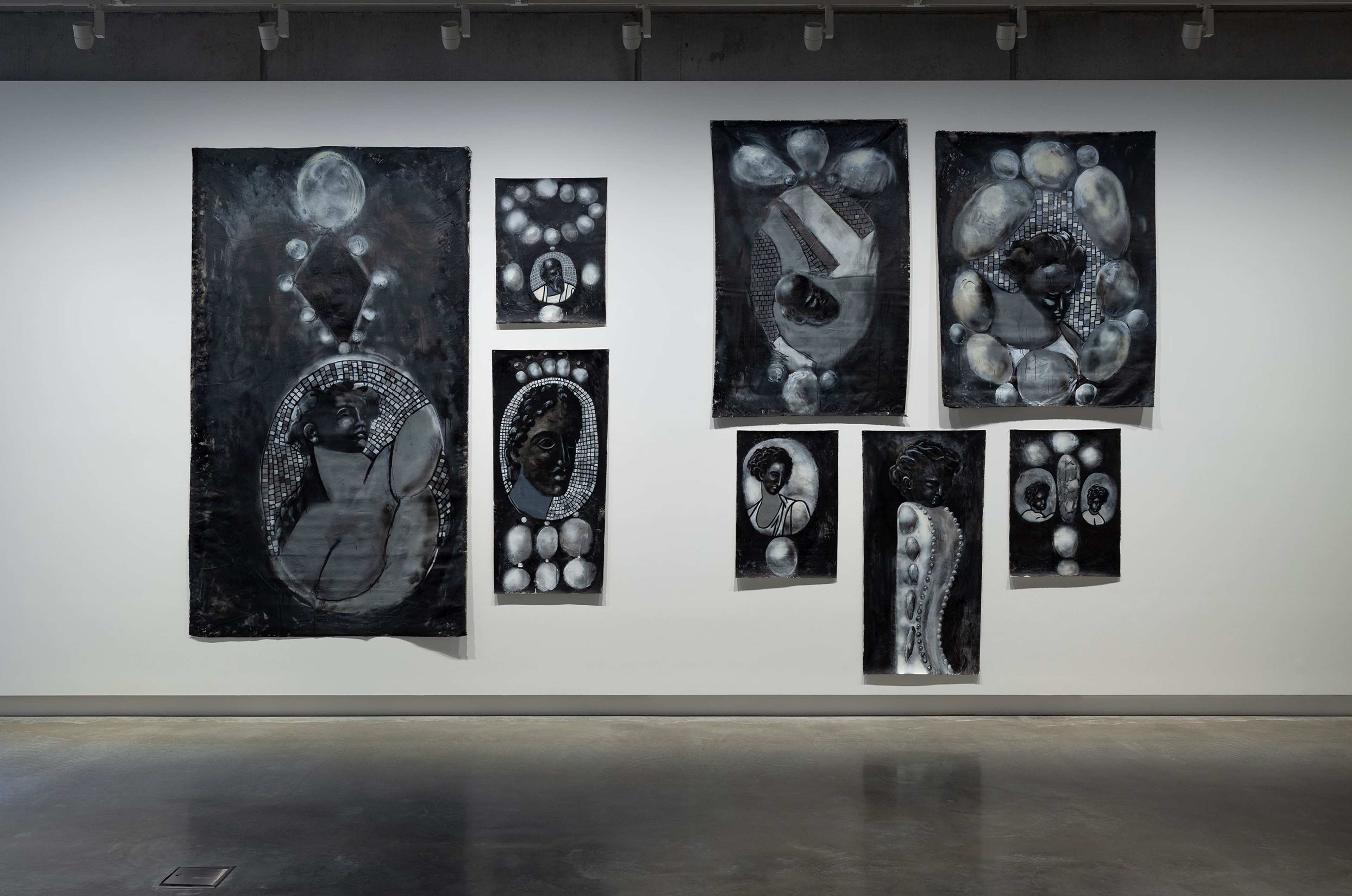 A gallery wall displays seven monochrome artworks featuring abstract and stylized portraits, circular patterns, and textured elements, each in shades of black, white, and gray, with a polished concrete floor below.