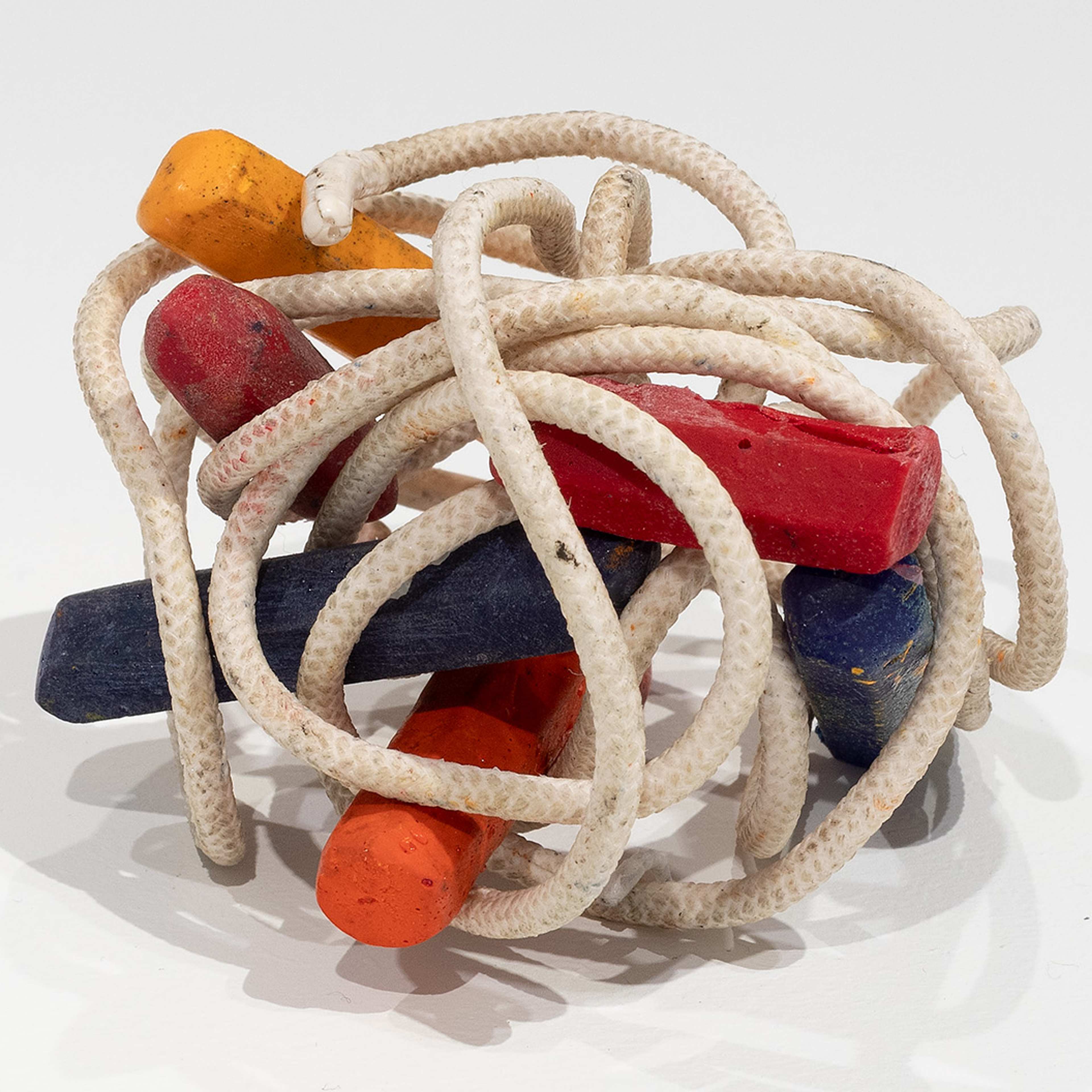 A tangle of white rope wraps around several colorful wooden sticks—red, orange, yellow, and blue—arranged in a loose, intertwined cluster on a white background.