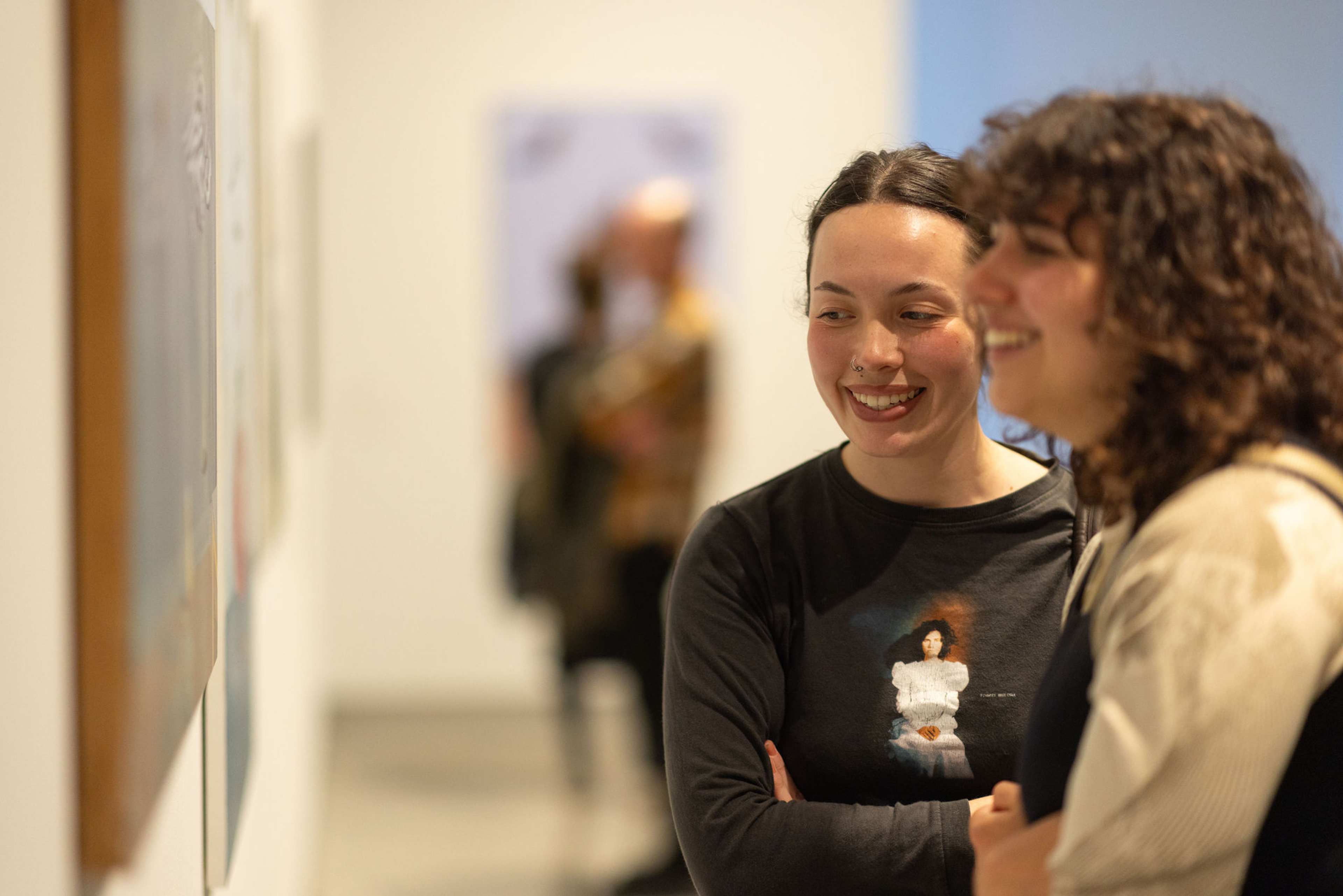 Two students look at art smiling in a gallery
