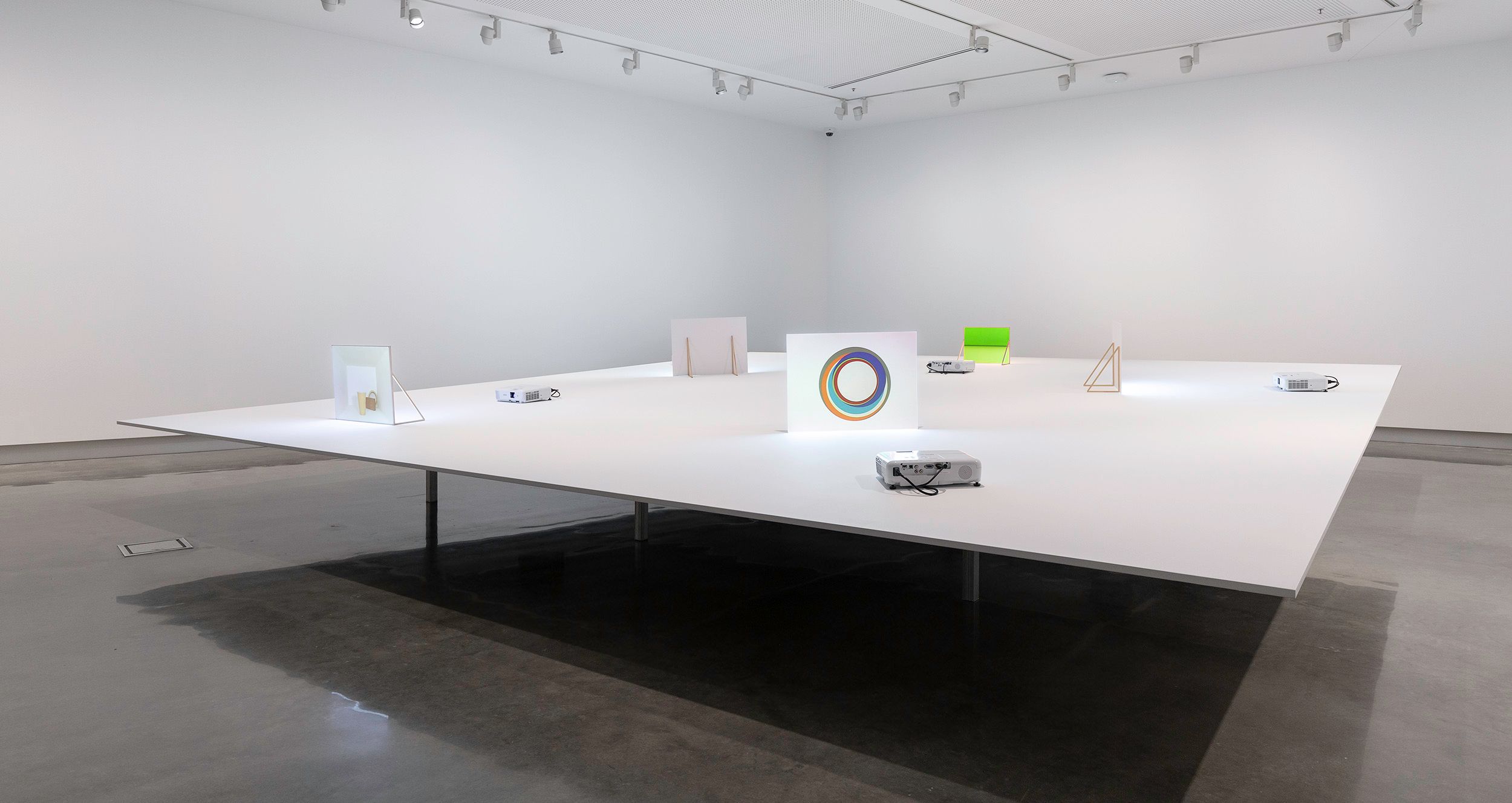 Installation in a white cube gallery, with various projections on objects on top of a large white table.
