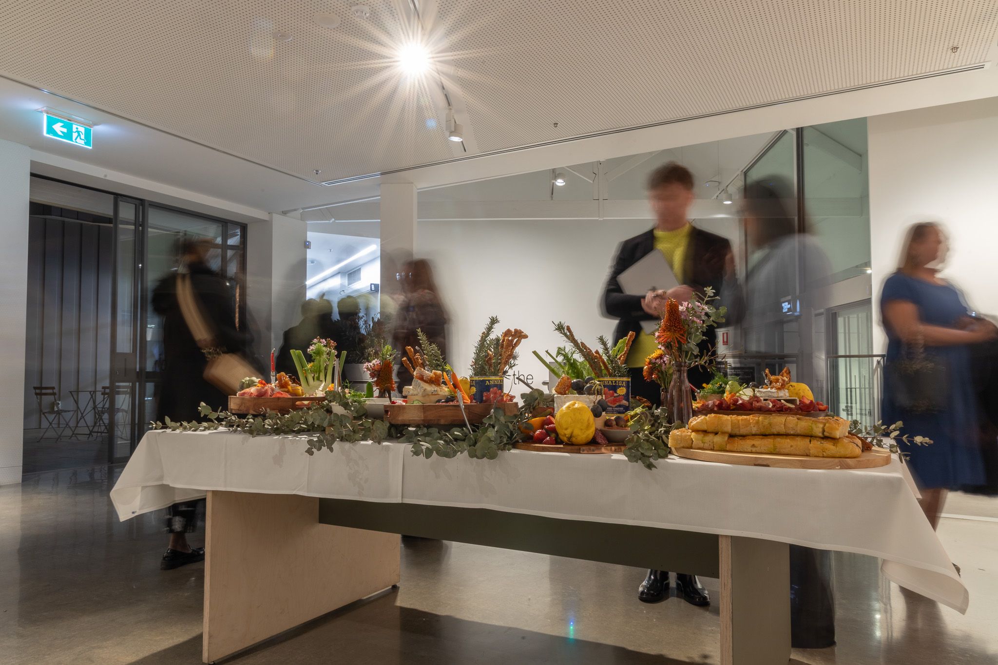 A table of colourful and delicious finger food on a white tablecloth. Blurred people move in background
