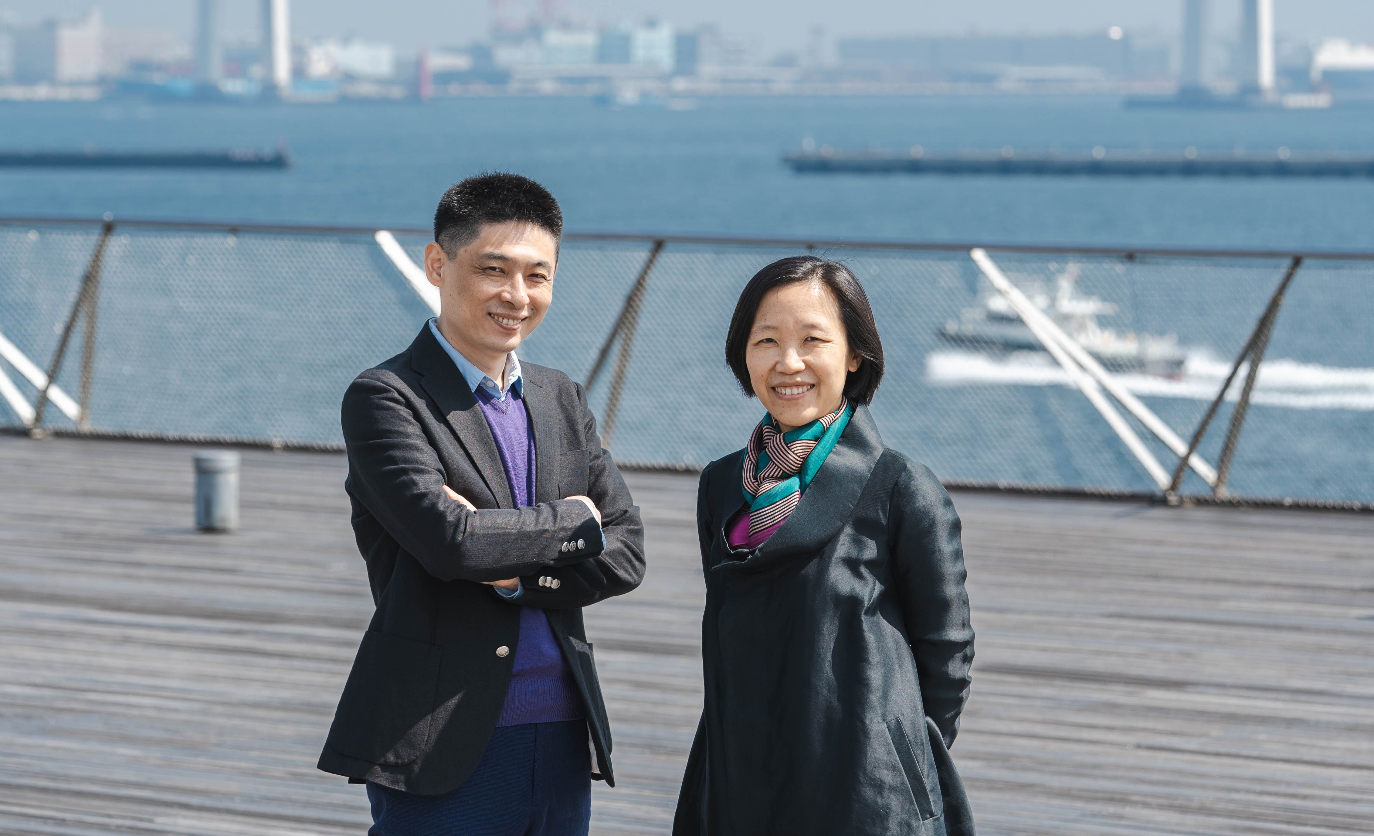 Liu Ding and Carol Yinghua Lu standing outside on a balcony by water.