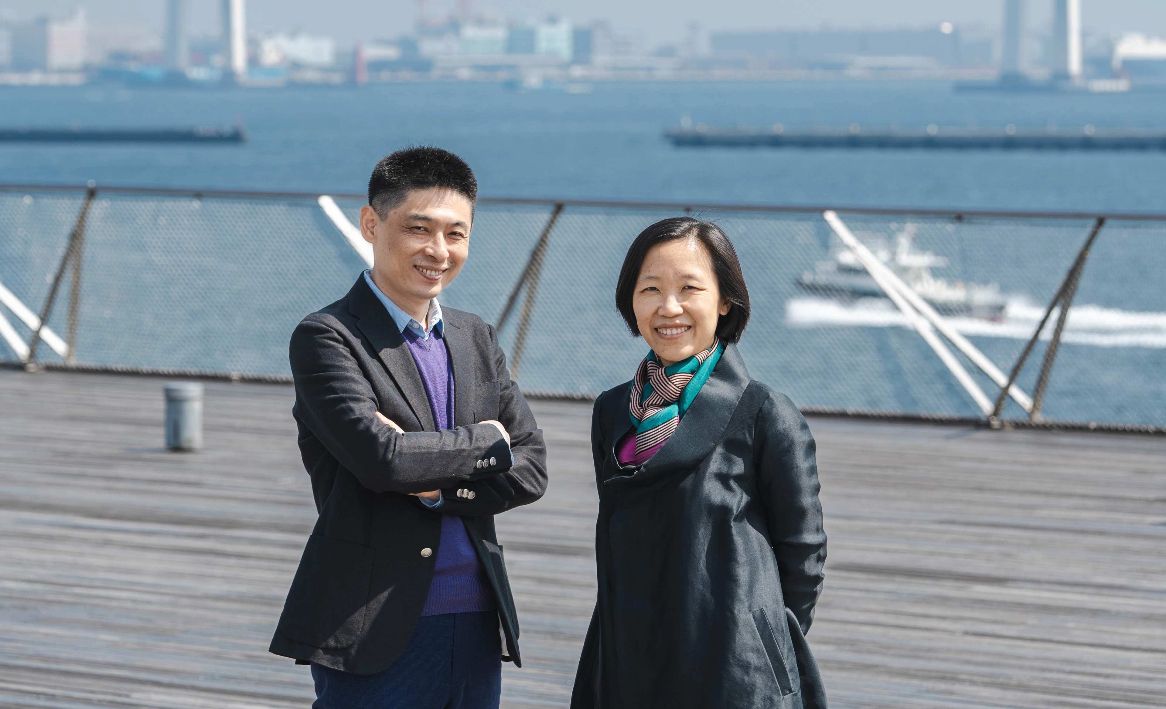 Liu Ding and Carol Yinghua Lu standing outside on a balcony by water.