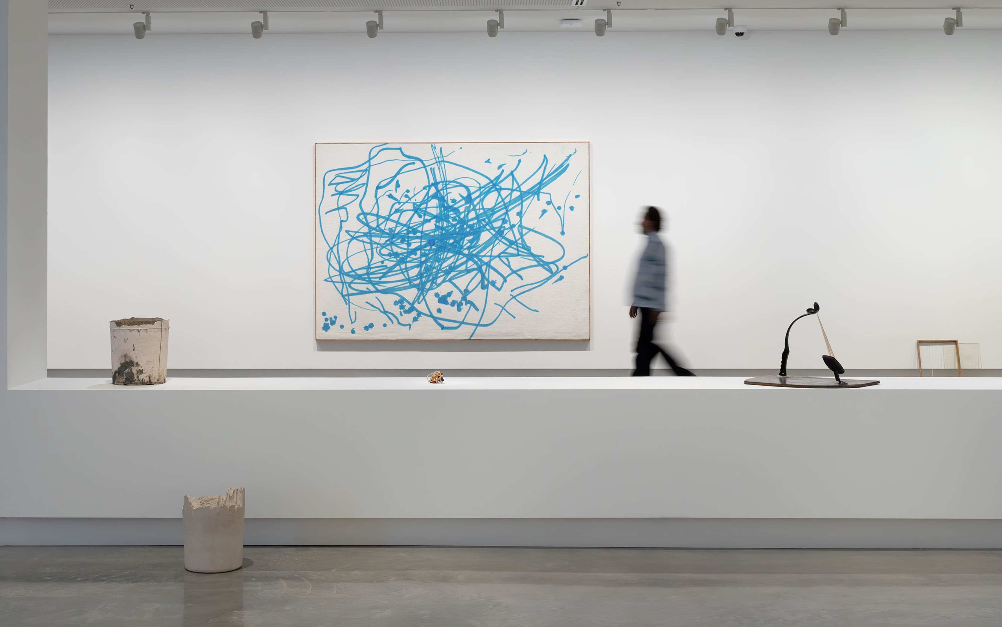 A person examines a blue and white scribble painting in a modern, spacious art gallery with polished floors.