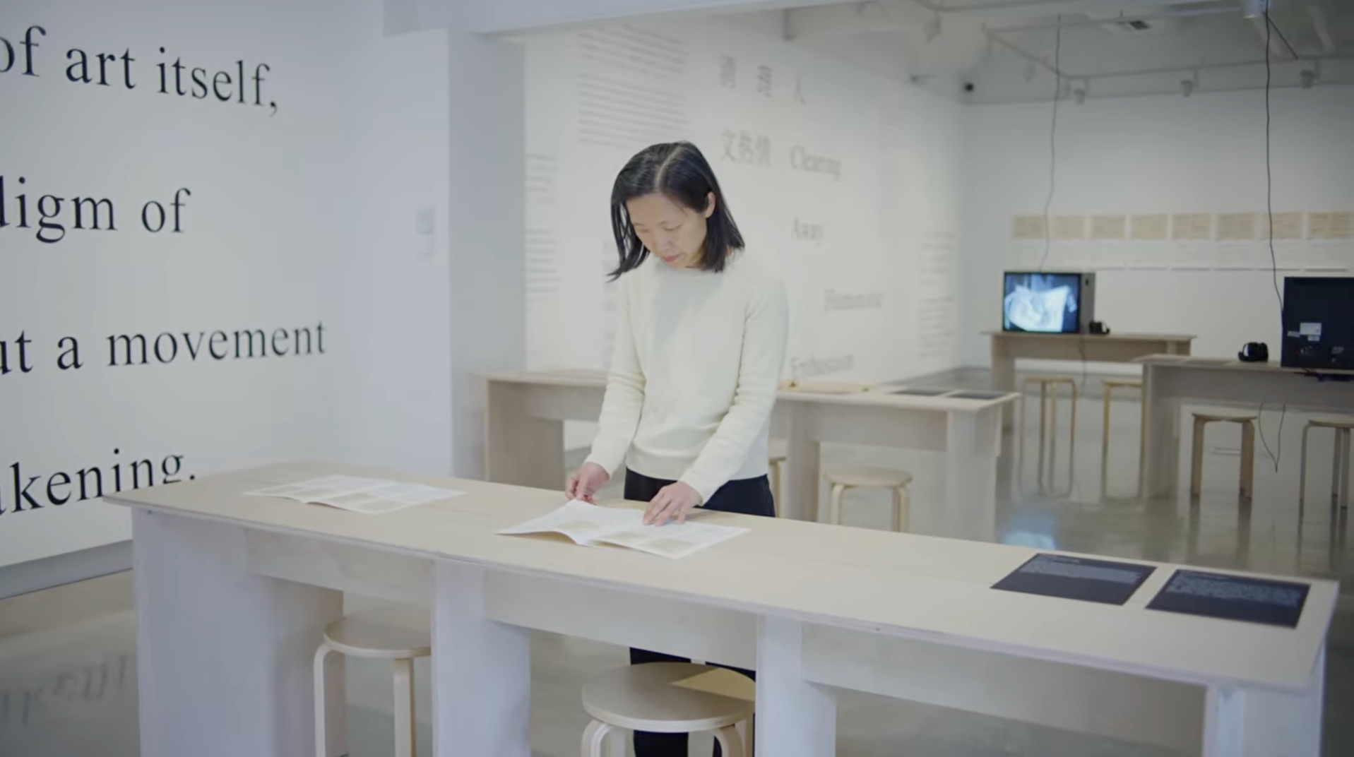 Dr Carol Yinghua Lu, flipping through a booklet on a wooden table in a gallery.