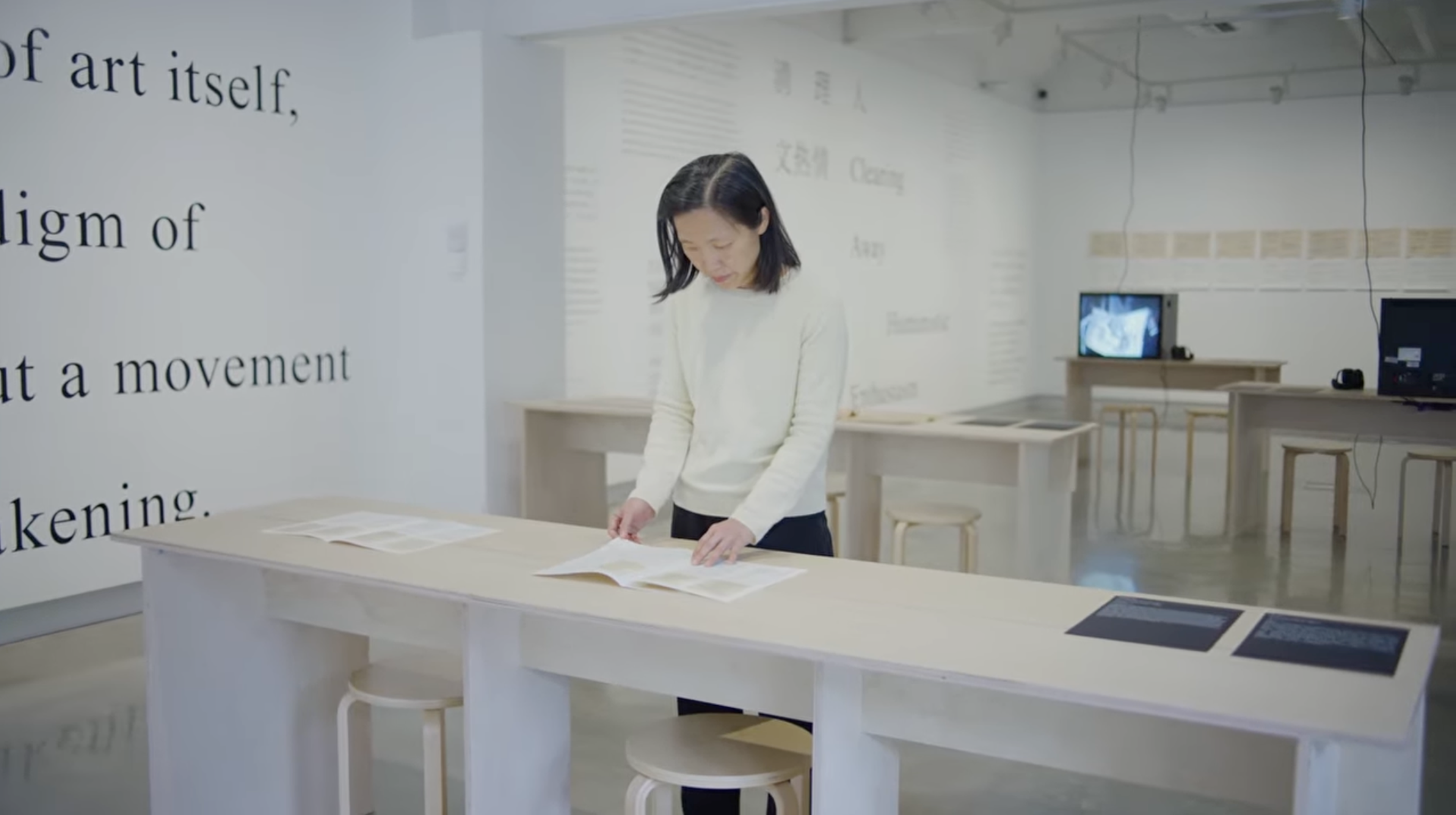 Dr Carol Yinghua Lu, flipping through a booklet on a wooden table in a gallery.