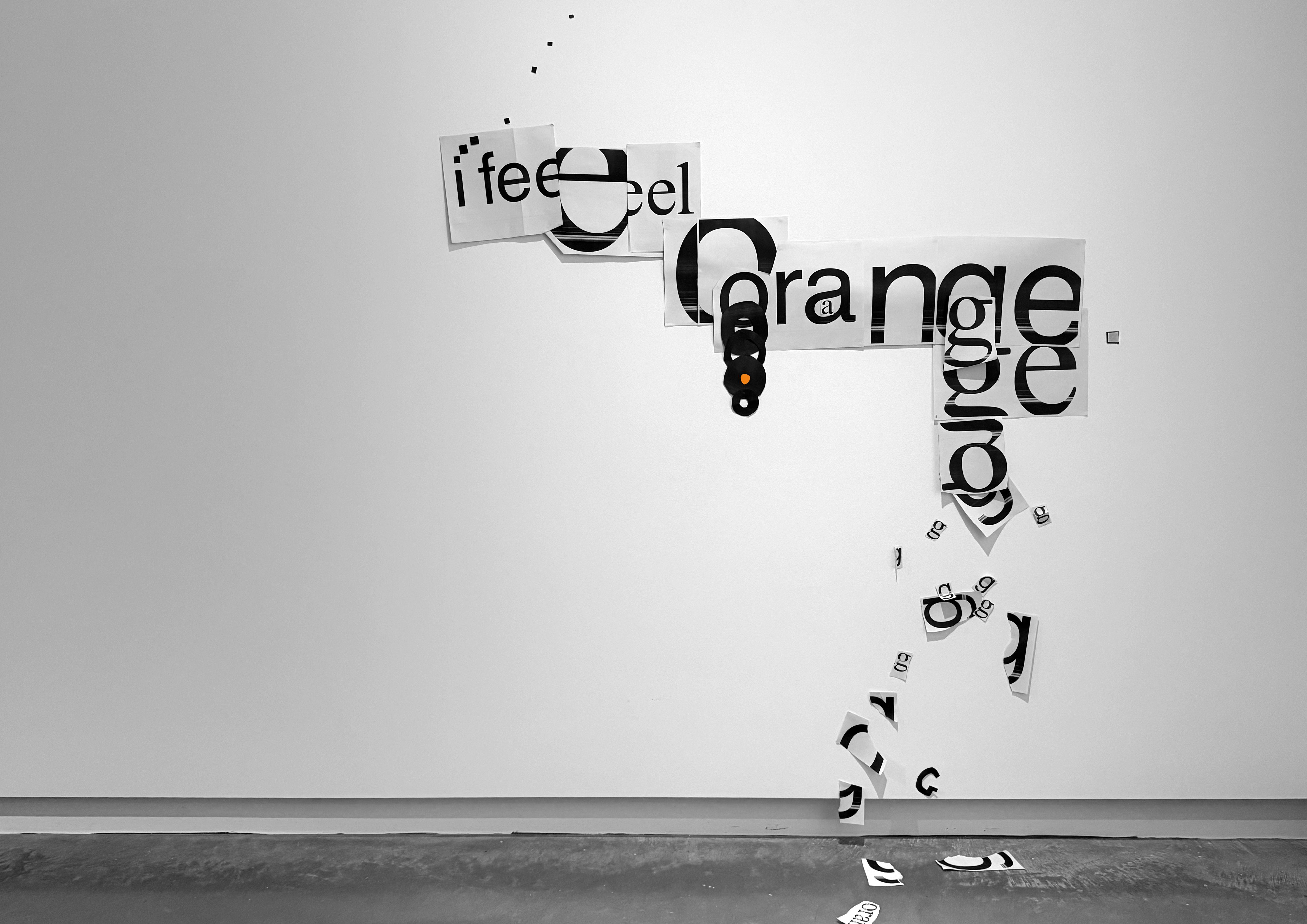 Cut out paper pasted to the wall loosely reads, 'i feel orange' 