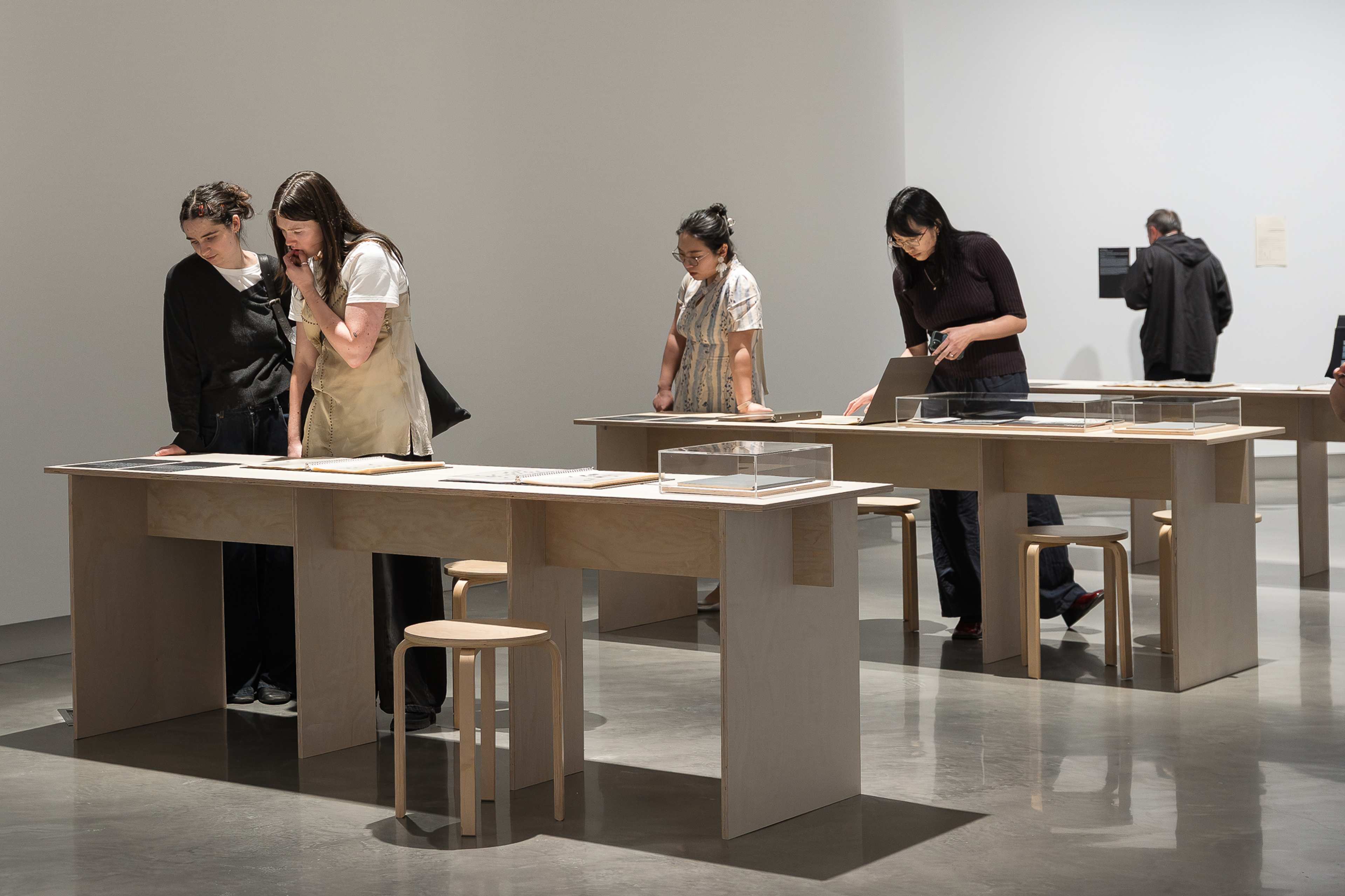 Various people looking at artworks laid out on rows of wooden tables.