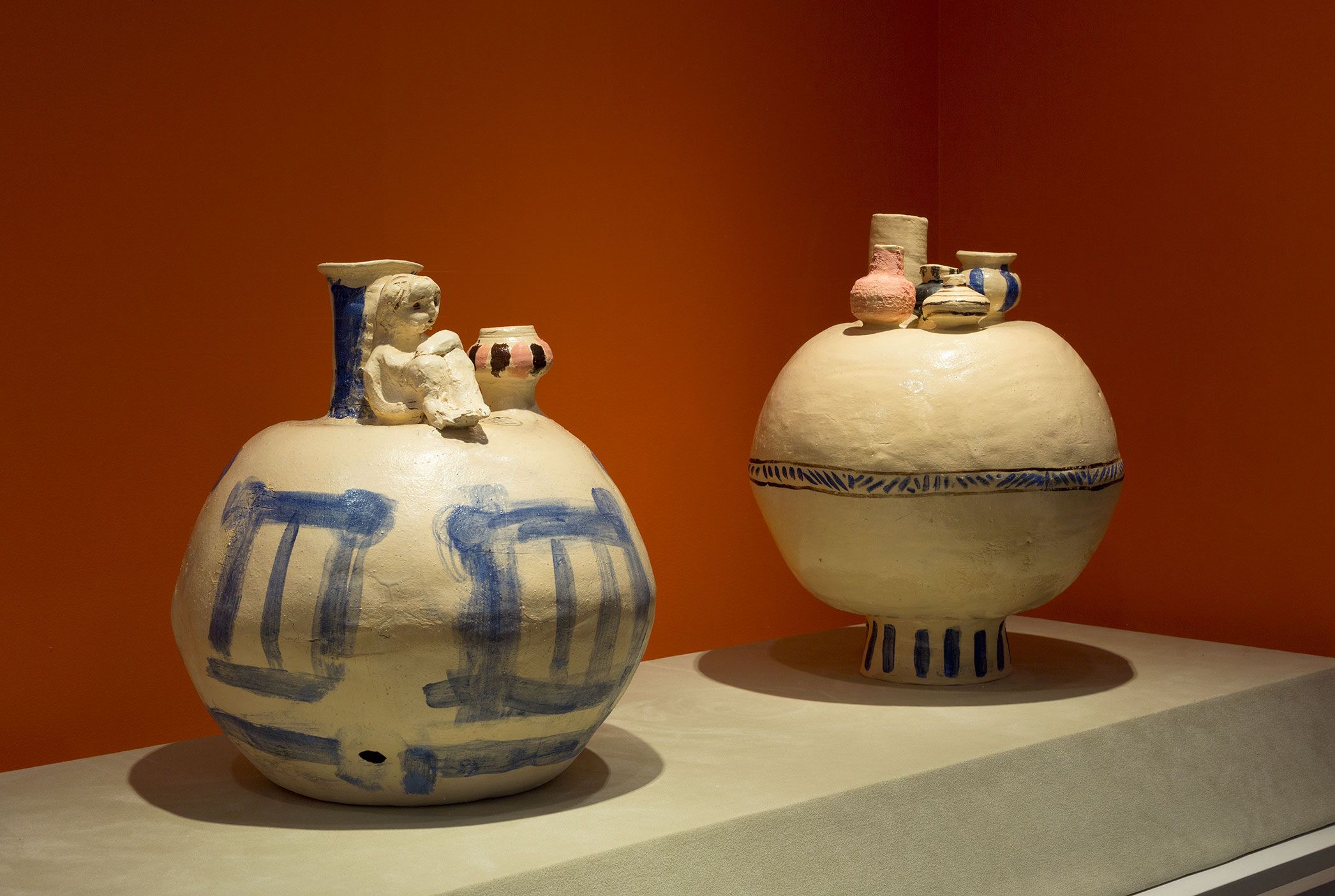 A photograph of two contemporary handmade ceramic vessels with rotund bodies and narrow necks featuring drawn shapes and sculpted figures attached to the vessels