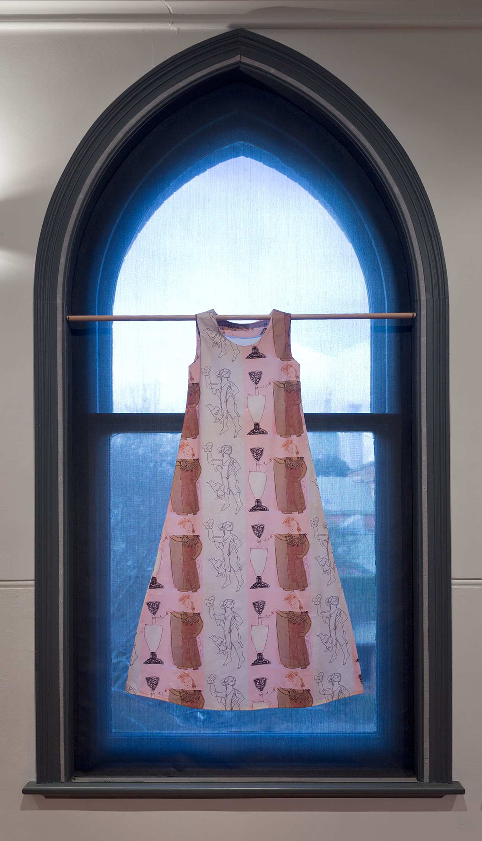 A photograph of a simple dress with a repeating graphic pattern hanging from a rod in an arched window