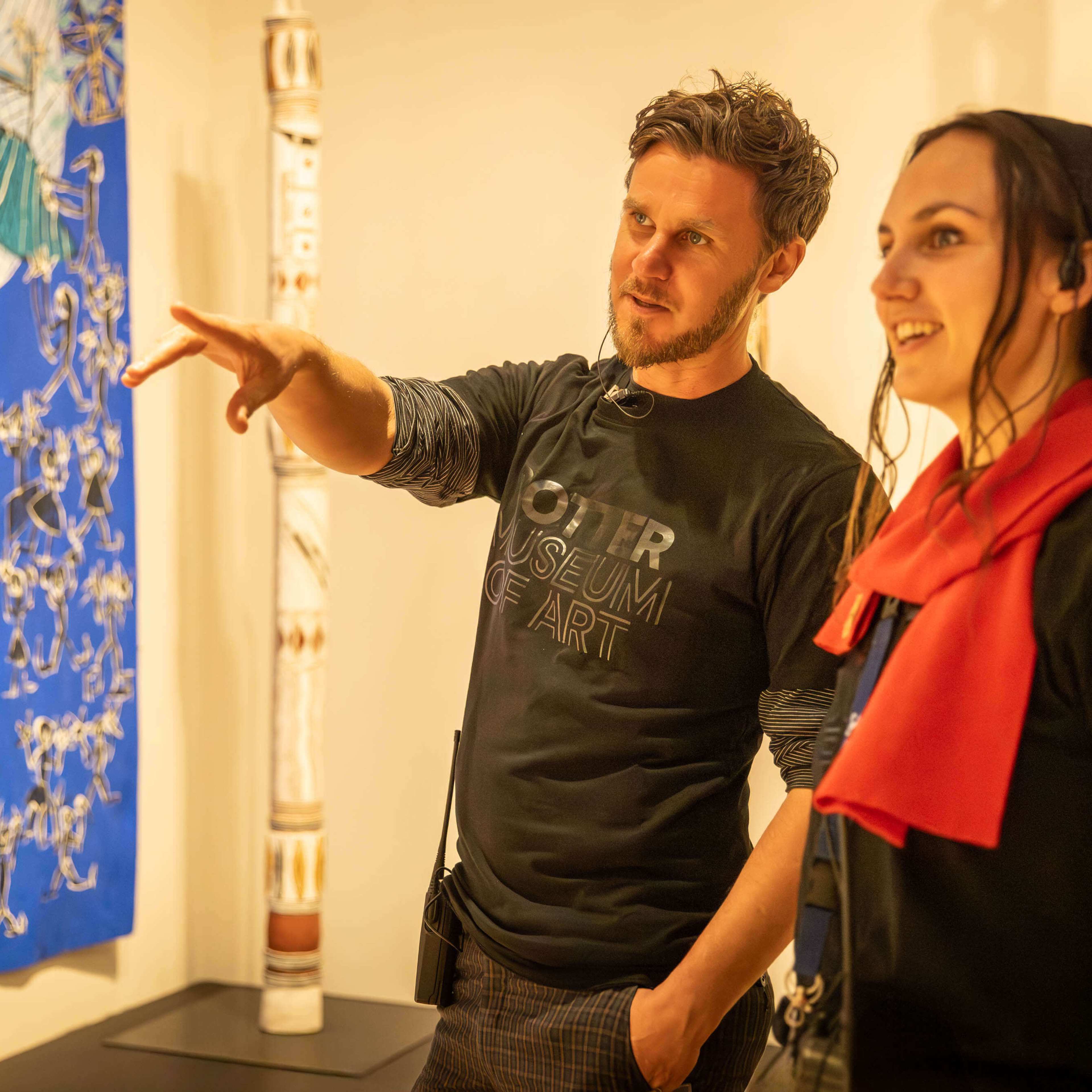 Tour guide points to artwork in the gallery with patron. A blue artwork hangs in the background.
