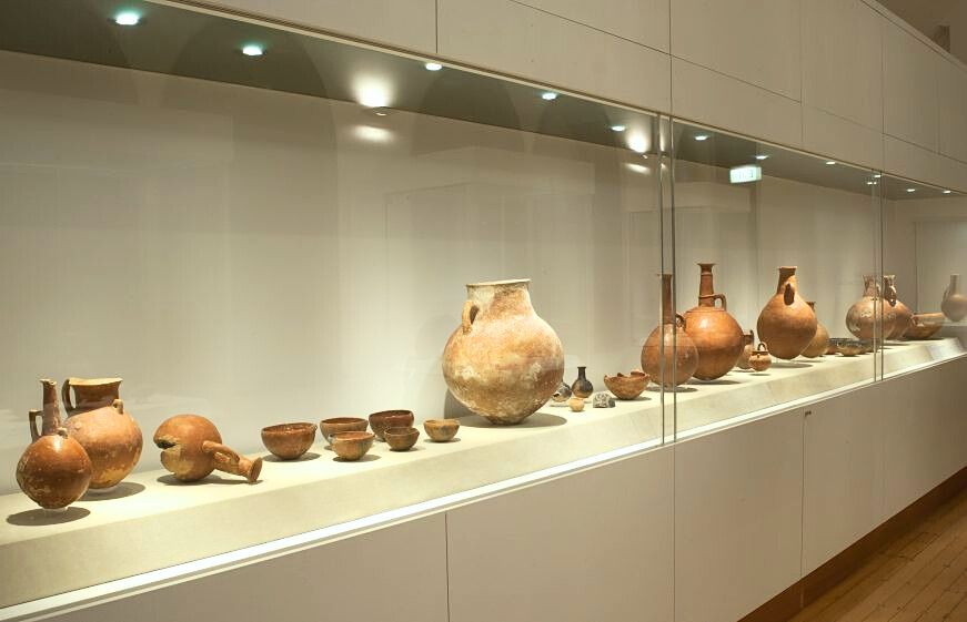 A photograph of a longe vitrine with a row of variously shaped terracotta vessels in it