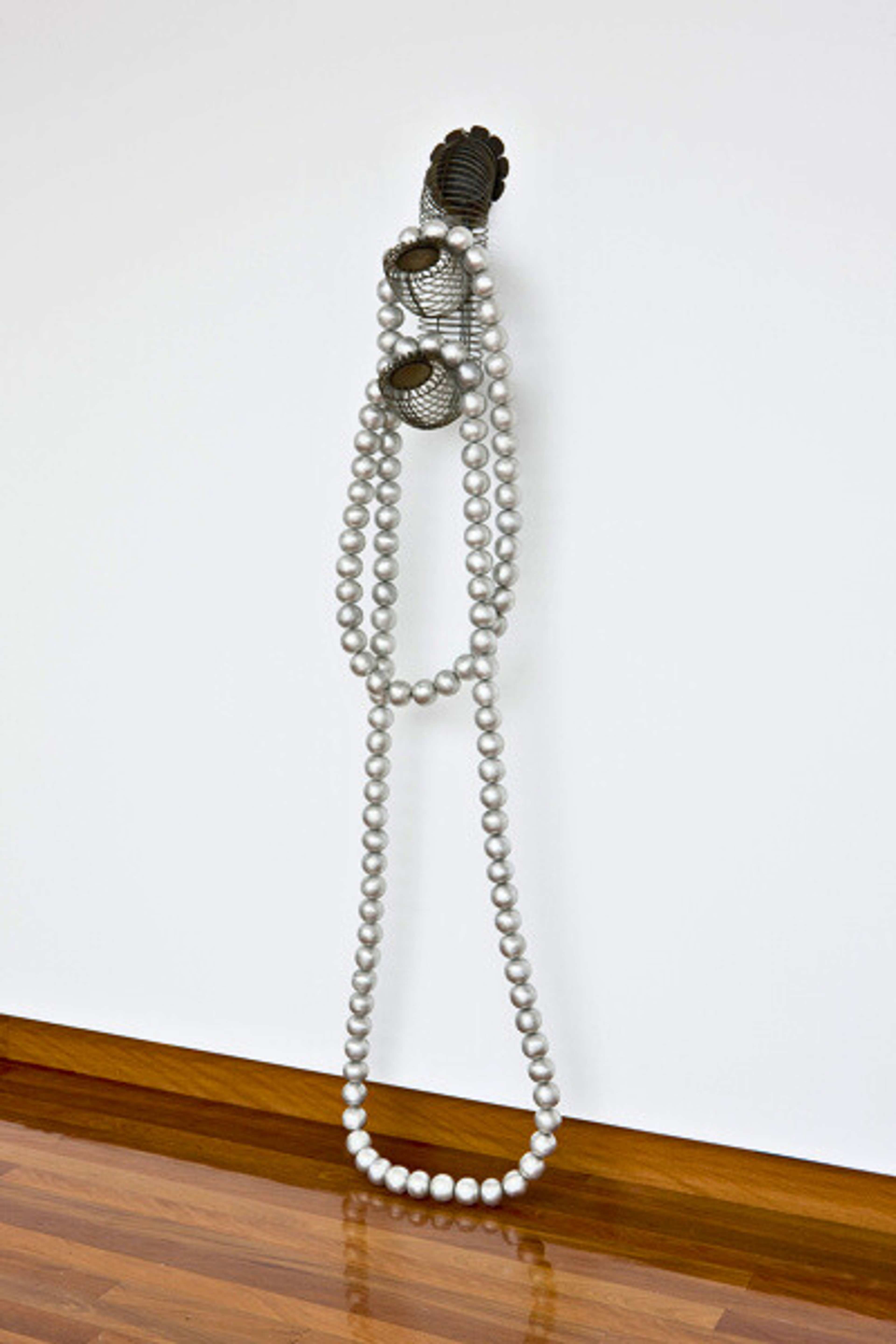 A photograph of a sculpture reminiscent of giant necklace on one wall of a gallery