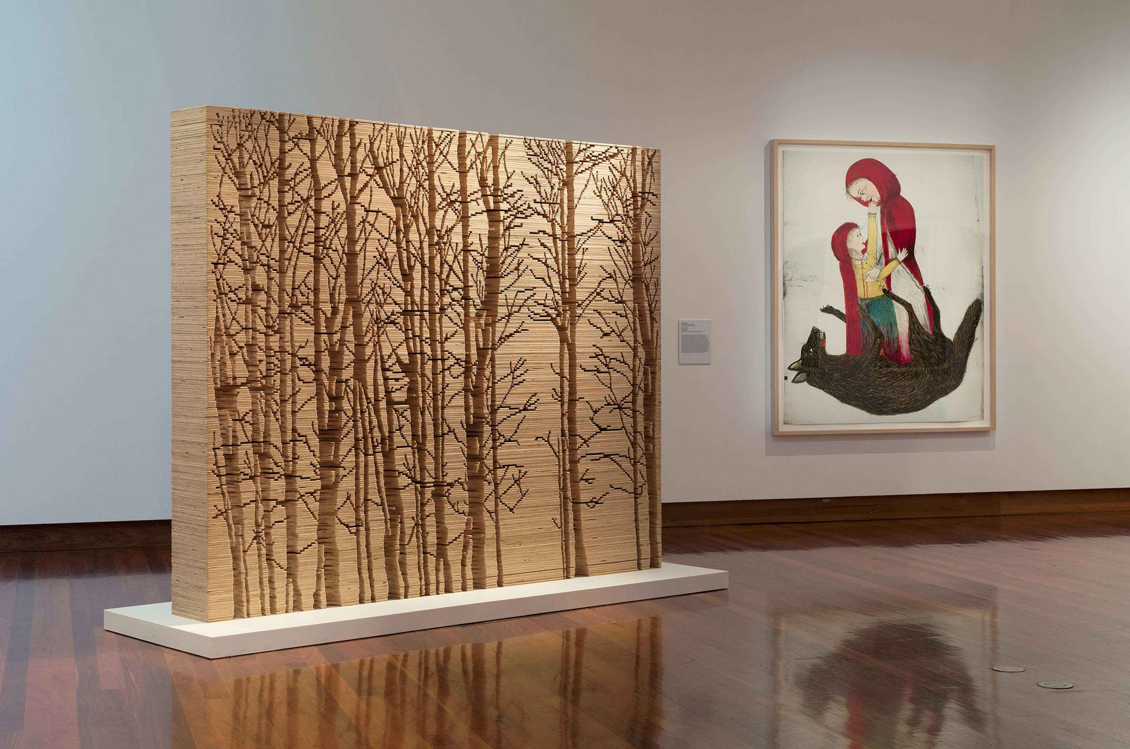 An image of little red riding hood with wolf and plywood sculpture with bare trees in a gallery
