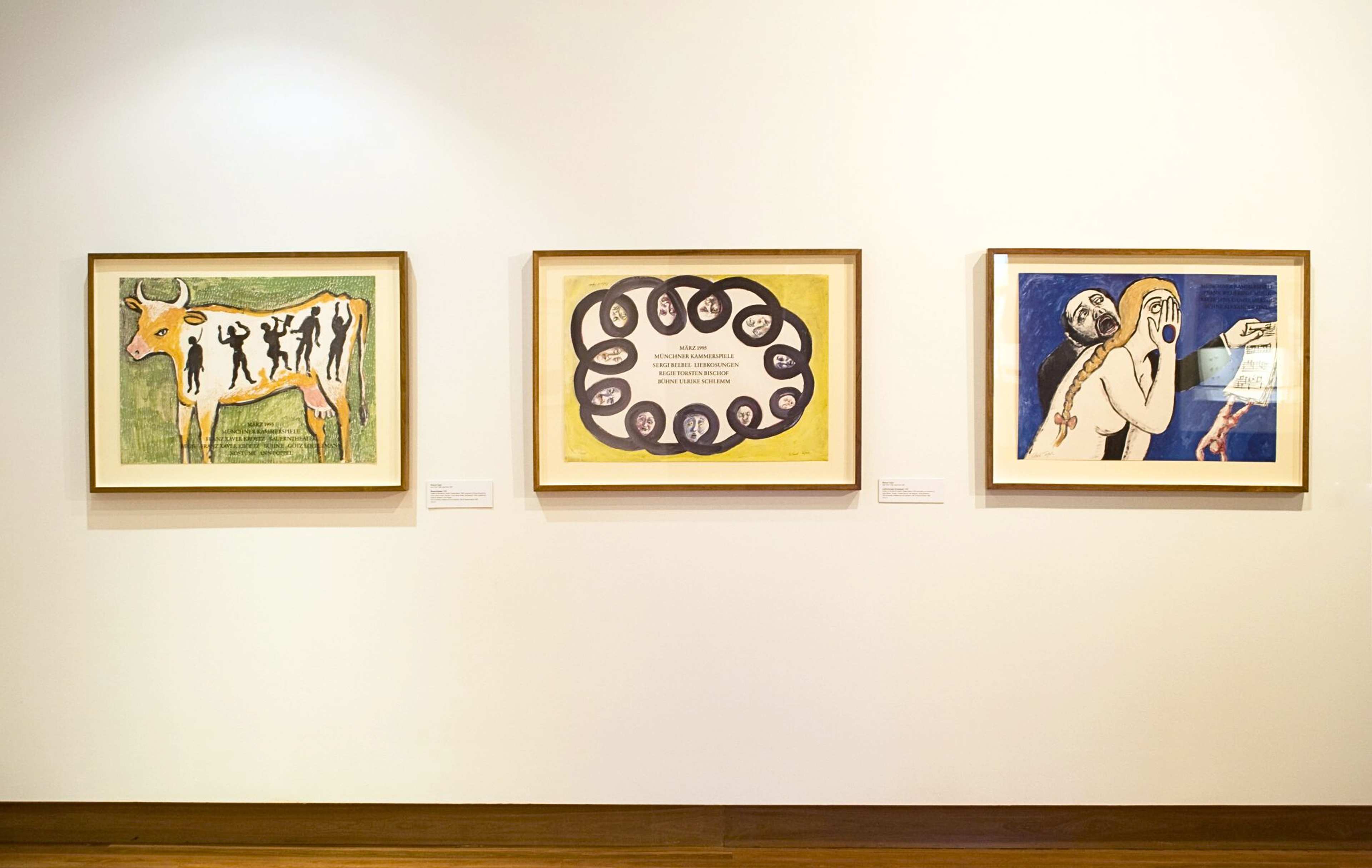 A photograph of a gallery wall displaying three colourful drawn posters