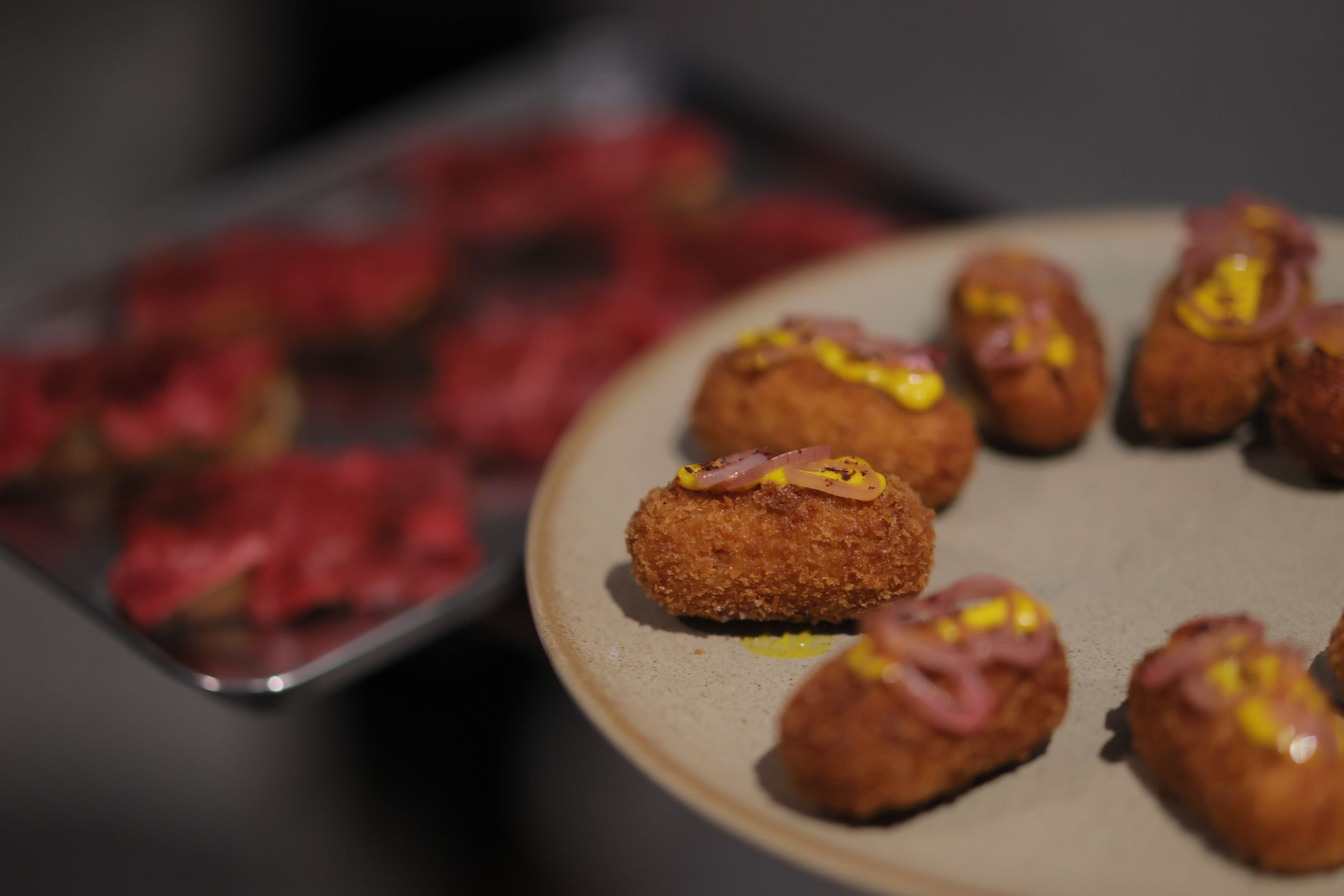 Croquettes with a yellow sauce are lined on a grey plate.