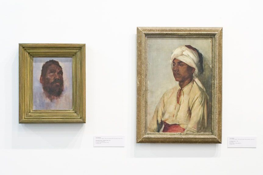 A photo of a gallery featuring two painted portraits of people of different etnicities