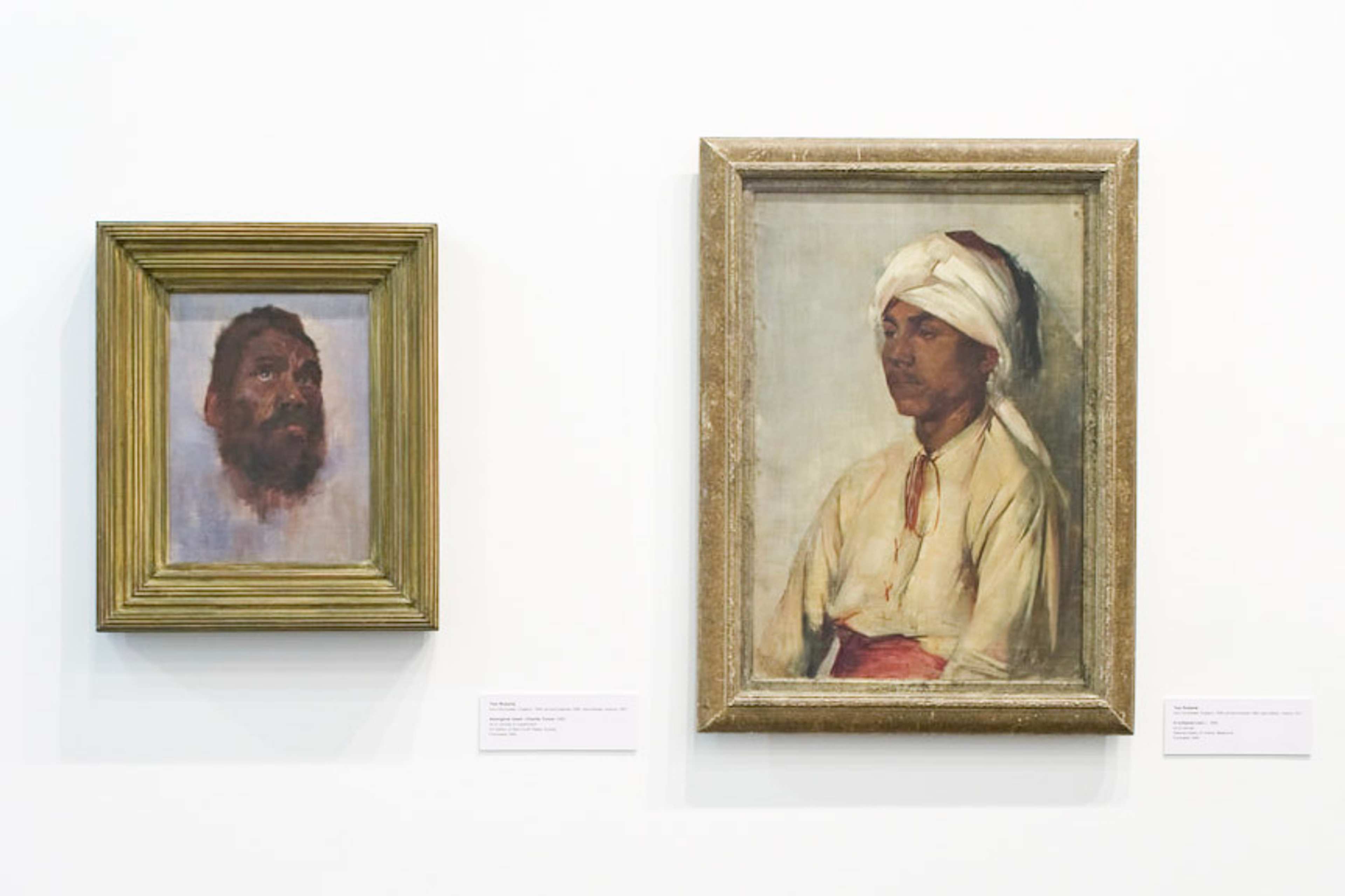 A photo of a gallery featuring two painted portraits of people of different etnicities