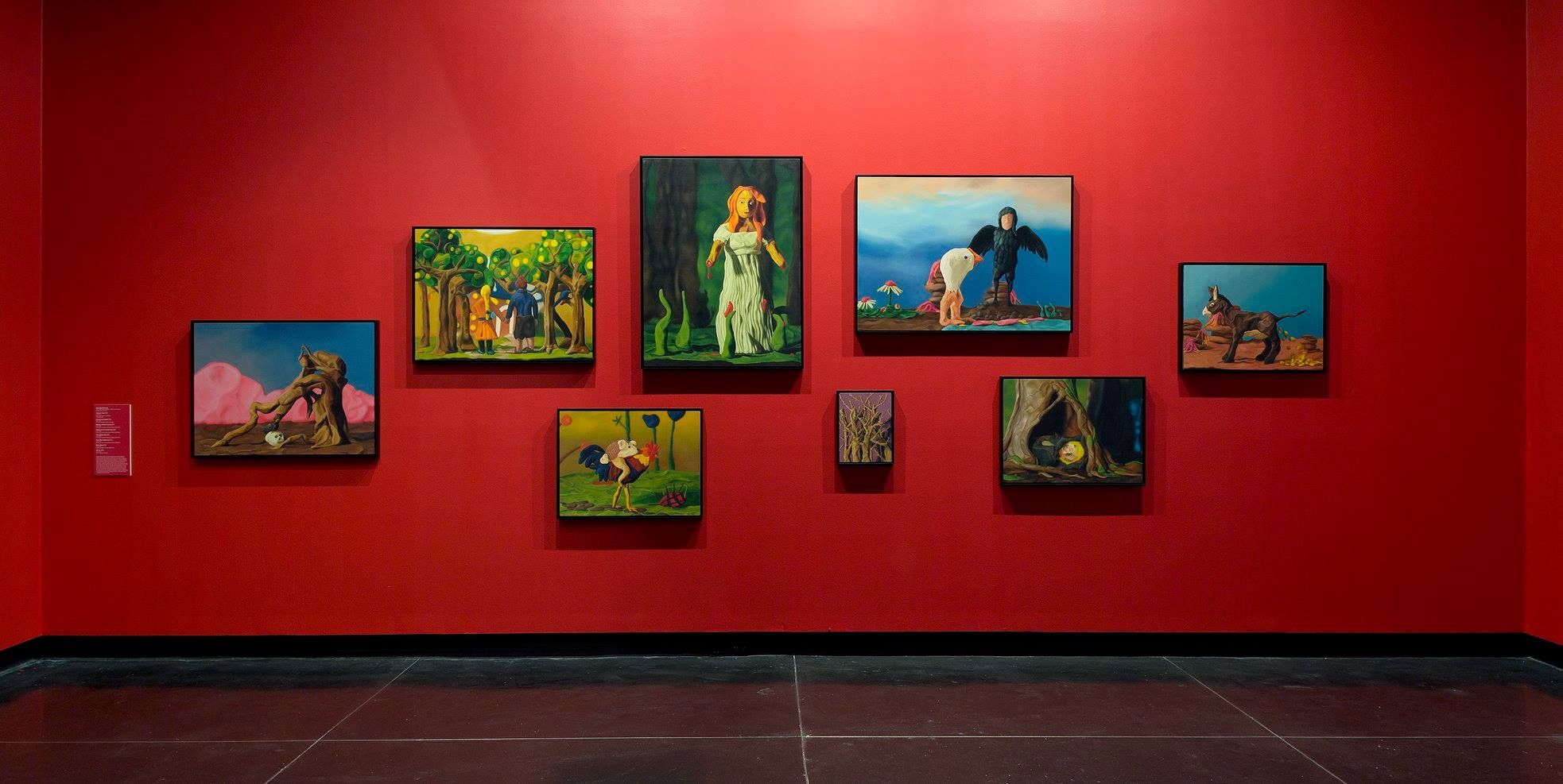 A salon hang of colourful paintings on a red-painted wall