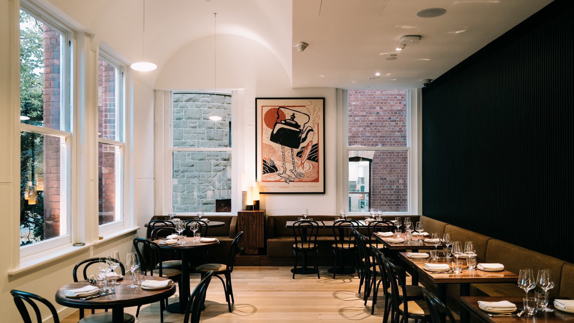 An empty restaurant with windows on two sides, wooden floor and set tables in a line
