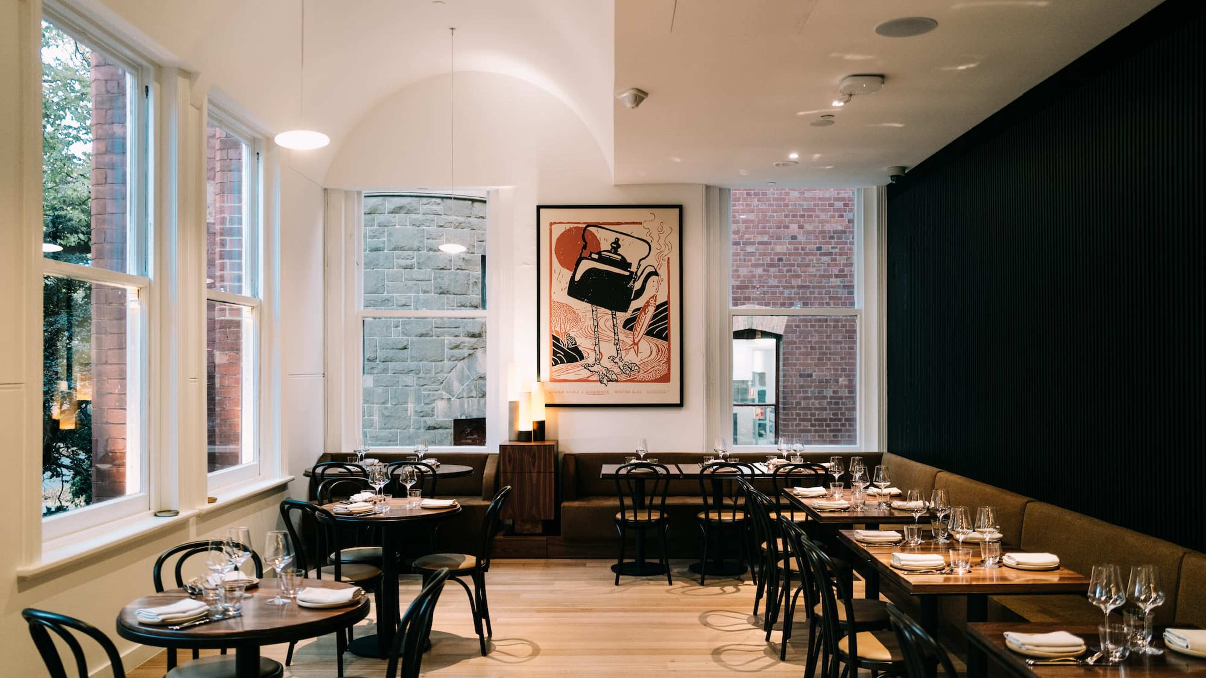 An empty restaurant with windows on two sides, wooden floor and set tables in a line