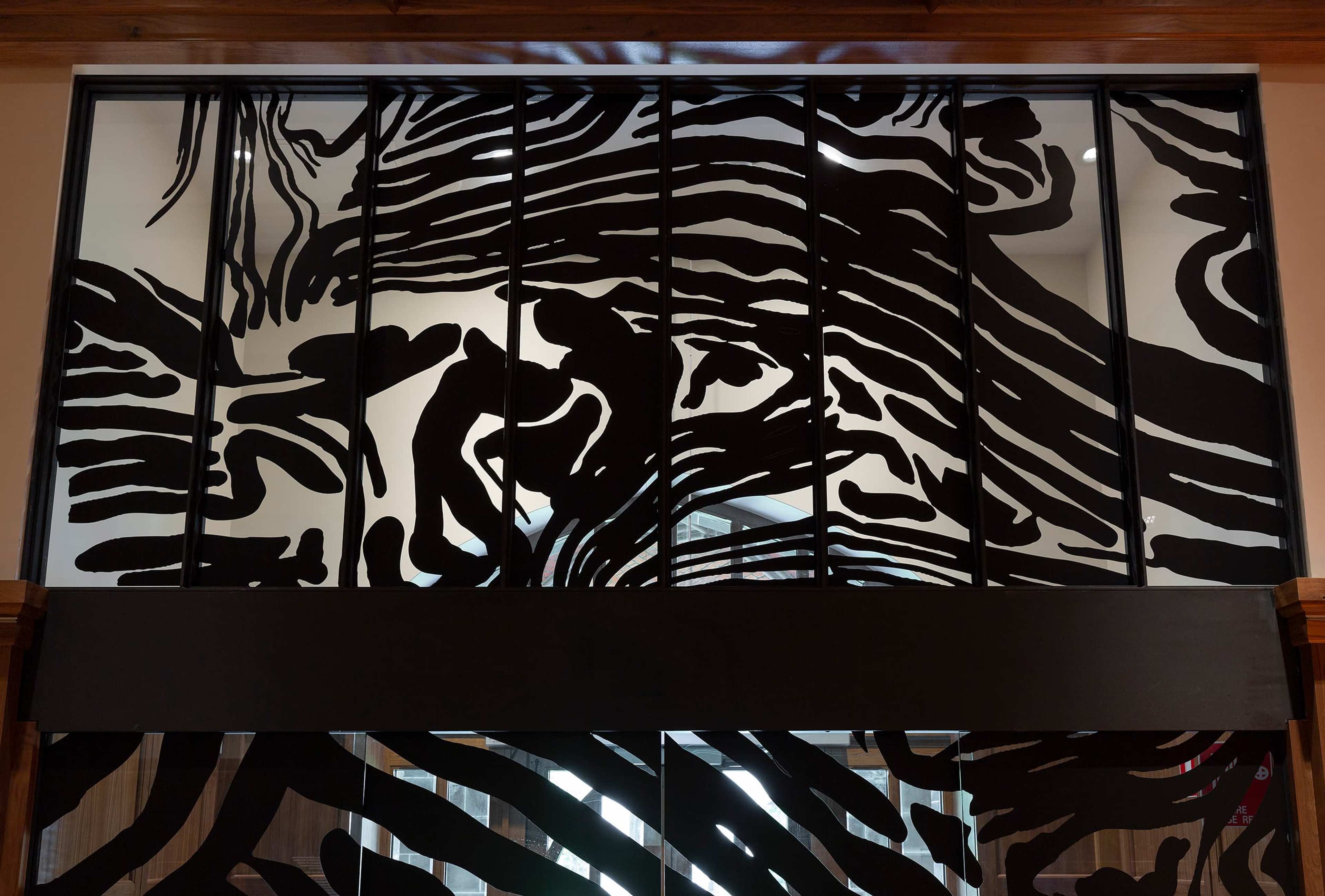 Large window panels featuring an abstract black and white design resembling zebra stripes, with light filtering through the glass and wood trim framing the top and sides.