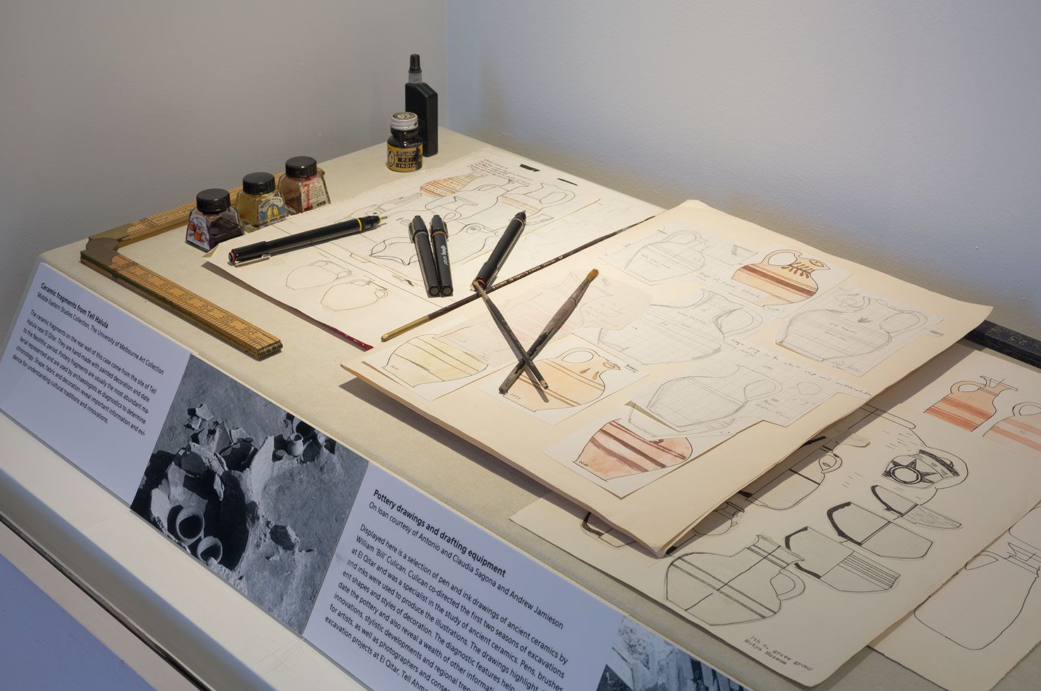 Drawings of pottery and drawing implements displayed in a museum cabinet