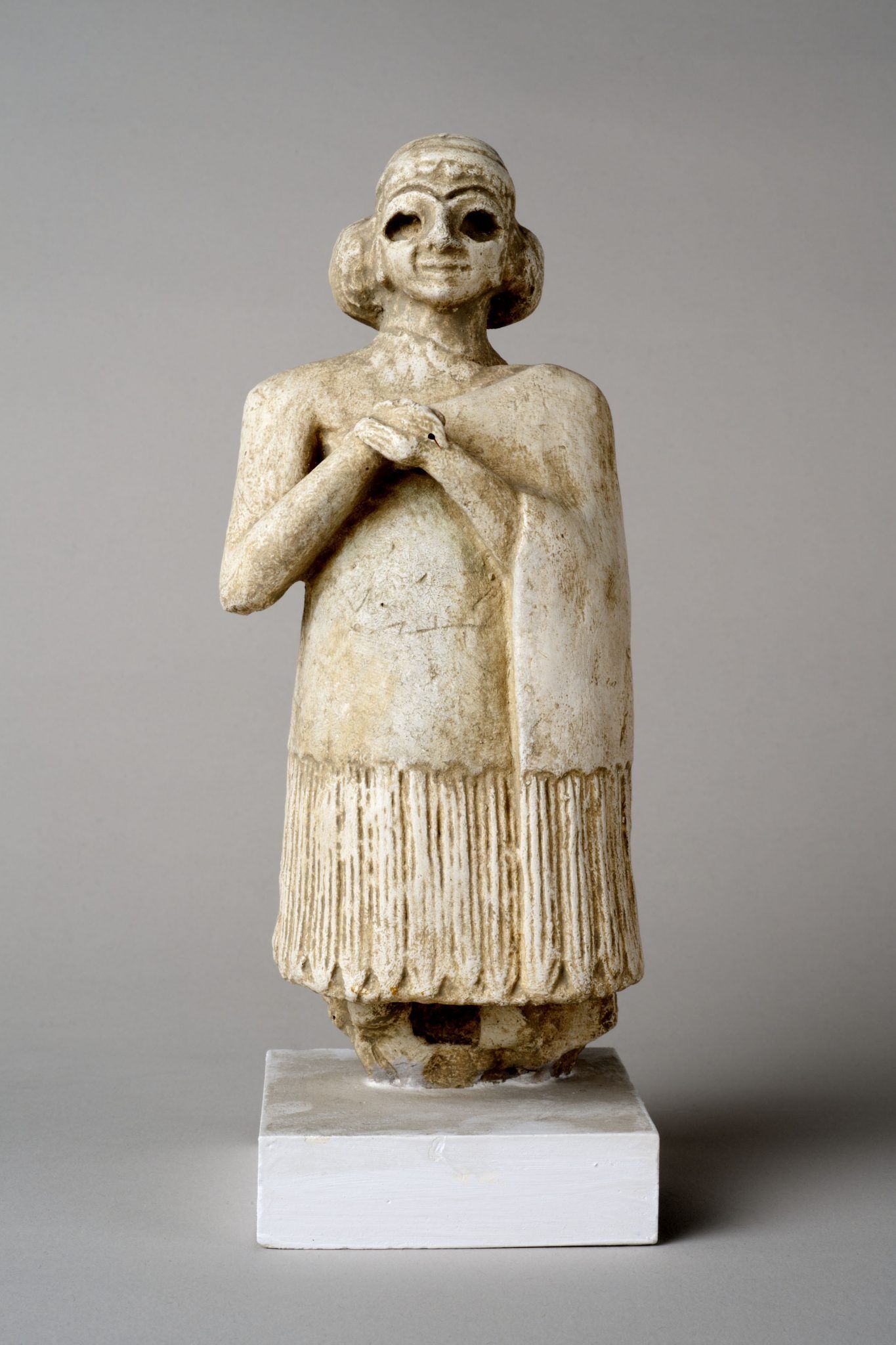 A photograph of an ancient figurine in a long coat and arms folded at chest