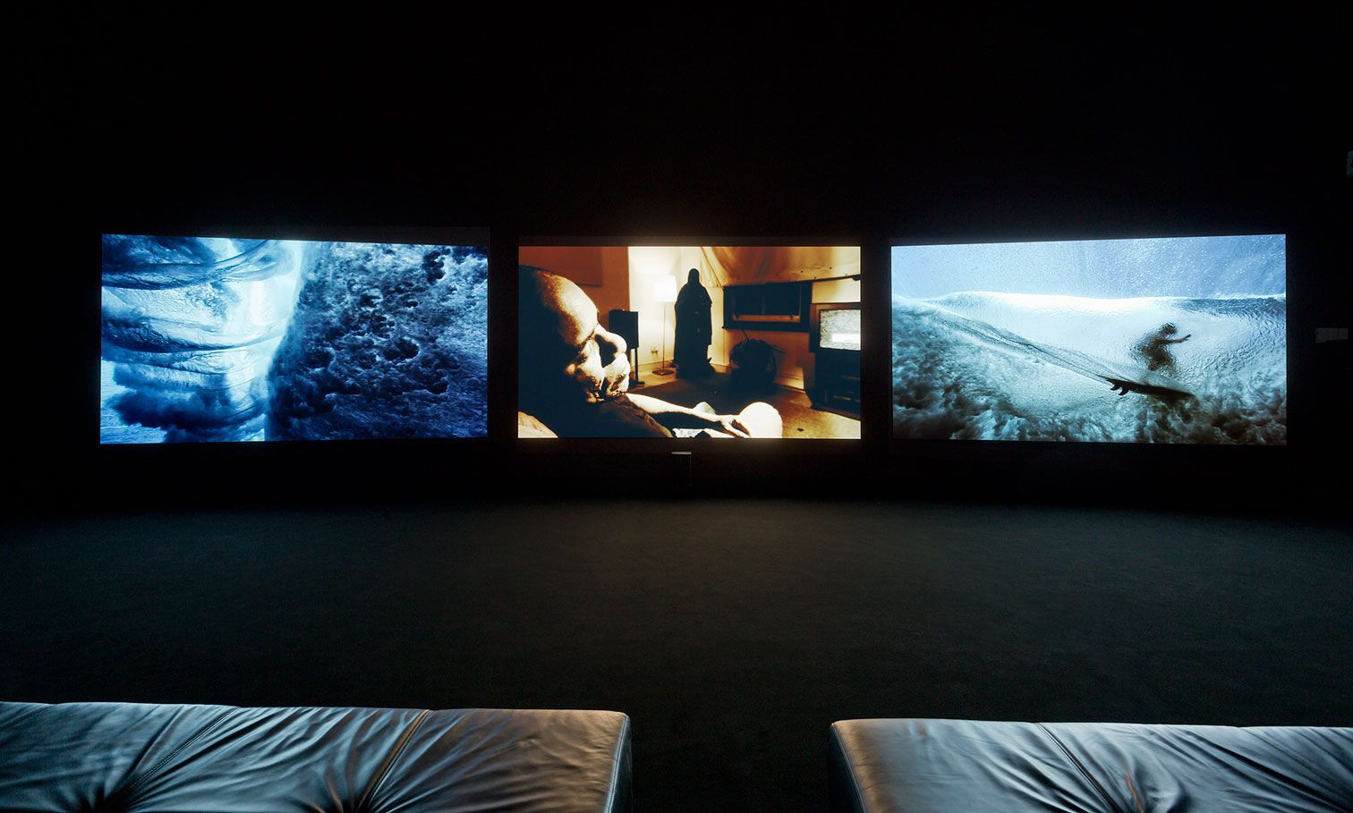 A three-channel projection of images featuring people and water displayed in a darkened room with seating