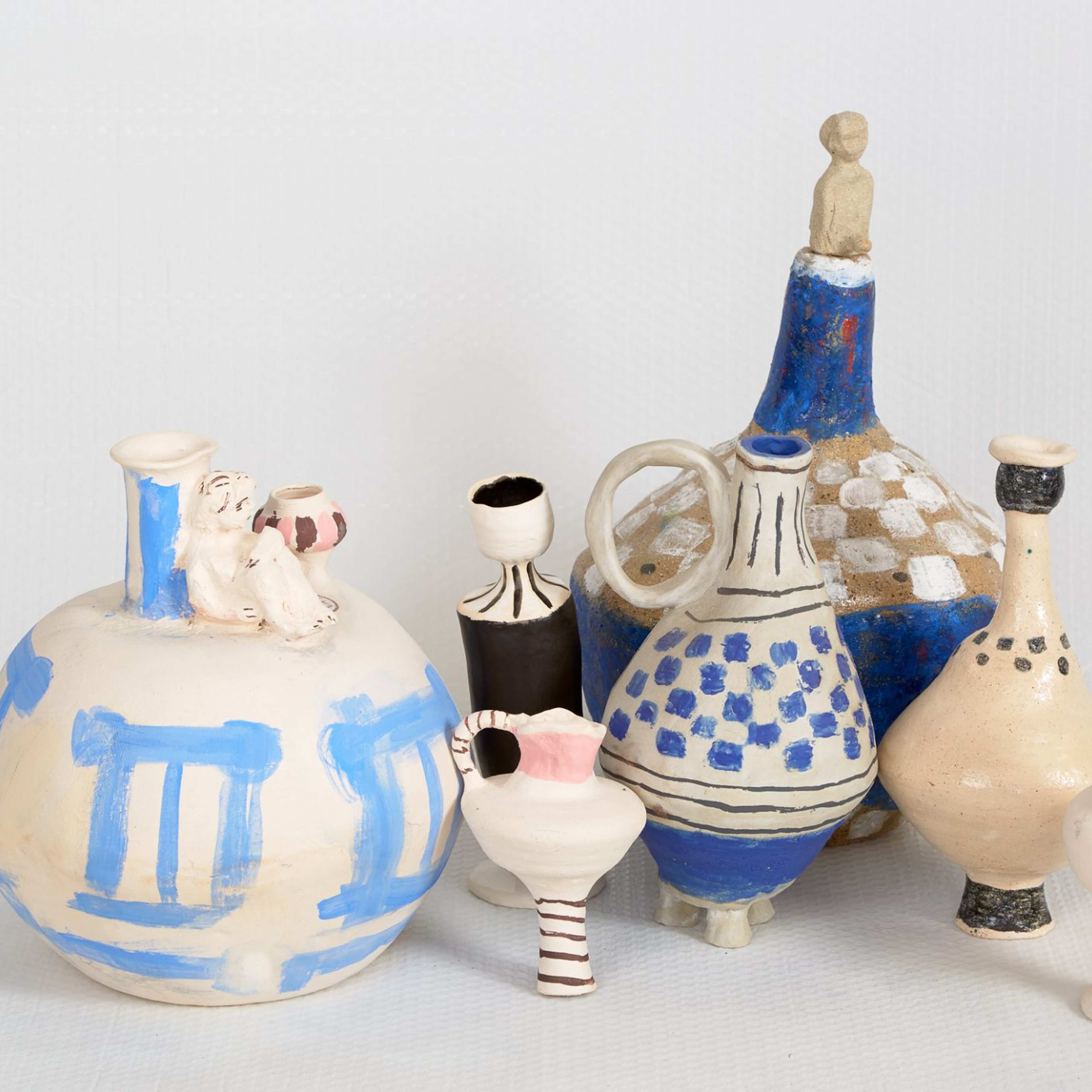 A cluster of ceramic hand-built vases and jugs with painted shapes in shades of off-white, blue, pink and black